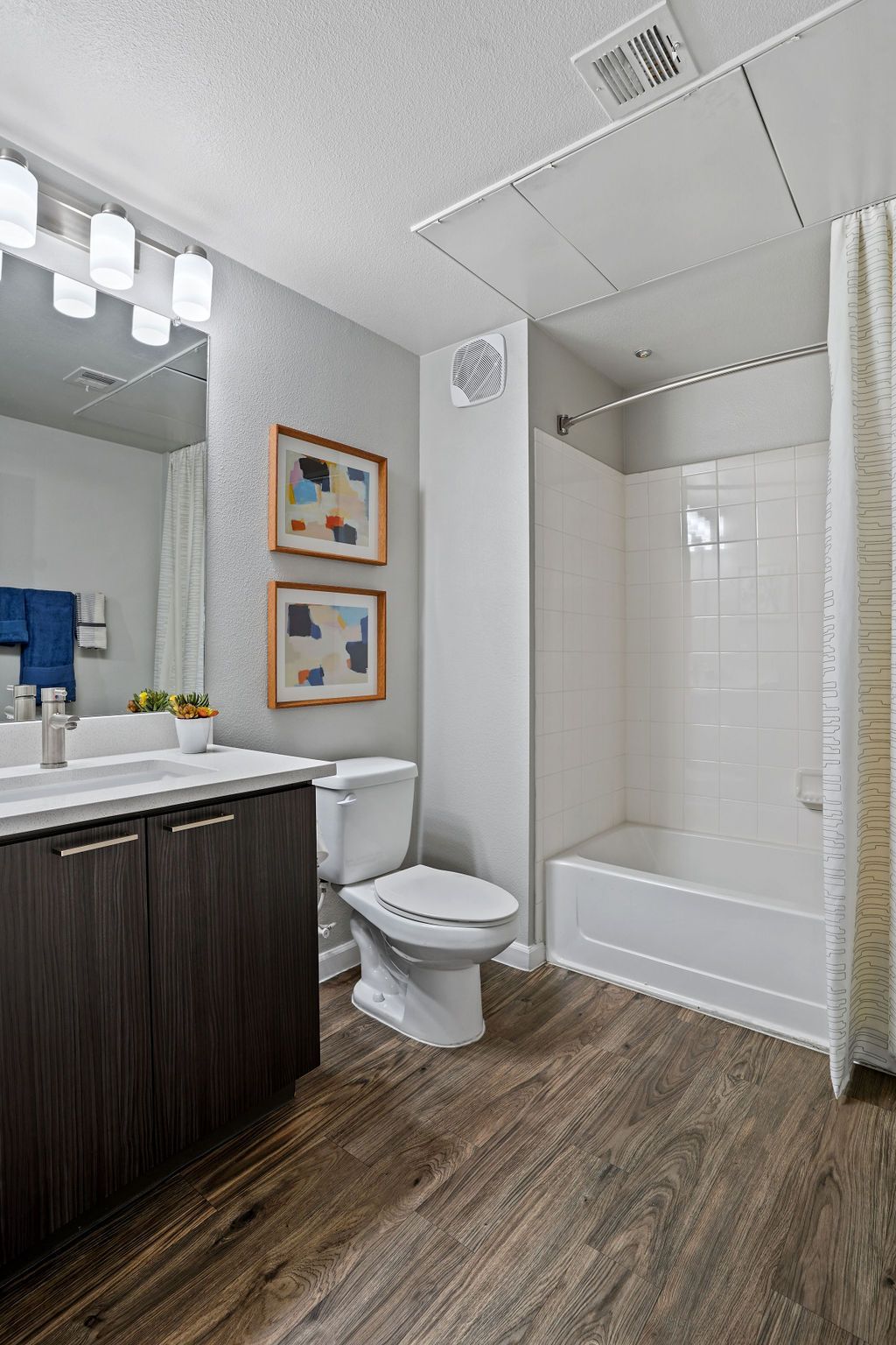 Bathroom in an apartment with a dark wood vanity, toilet, and white tiled bathtub/shower.