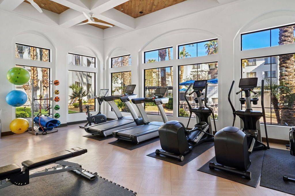 Bright on-site gym with treadmills, ellipticals, free weights, and large windows.