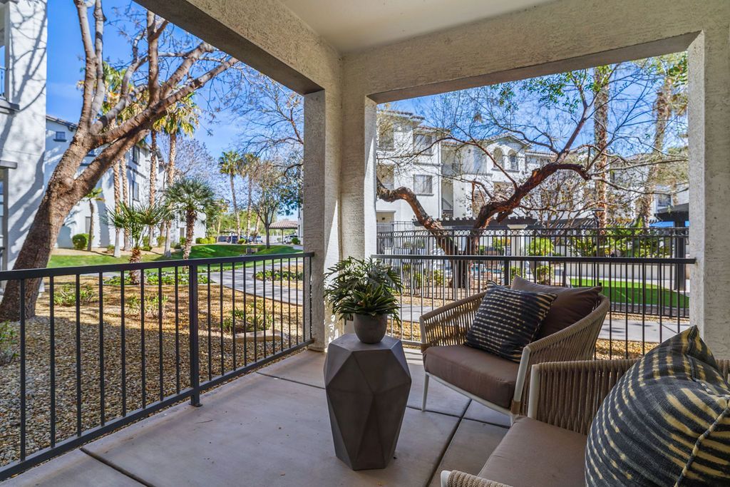 Balcony with wicker seating and a small table, overlooking a landscaped courtyard.