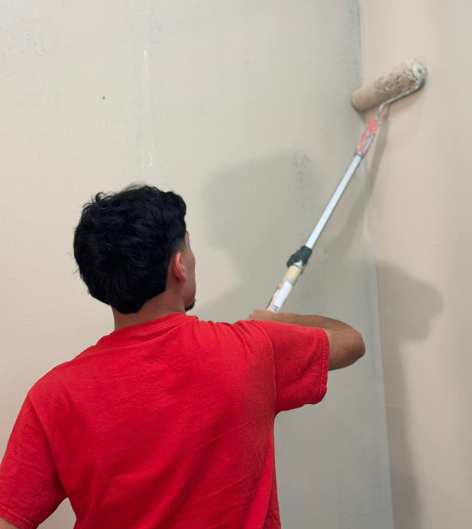 Person in red shirt painting wall with a roller and extender.