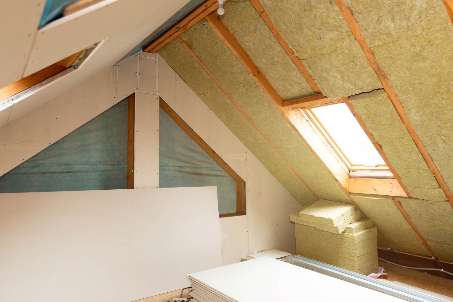 Interior view of an attic being renovated, showing exposed insulation, drywall, and a skylight.