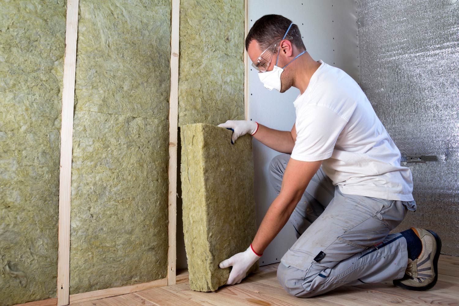 Person installs insulation in a wall, wearing a mask and gloves.