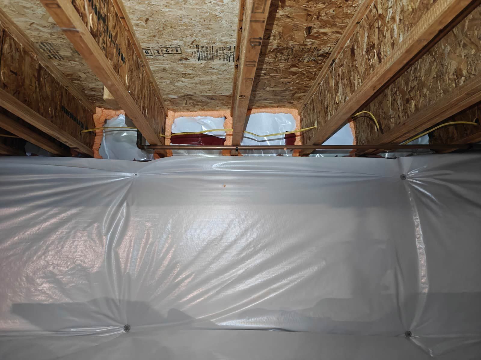 Person in protective gear sprays foam insulation onto a wooden wall.