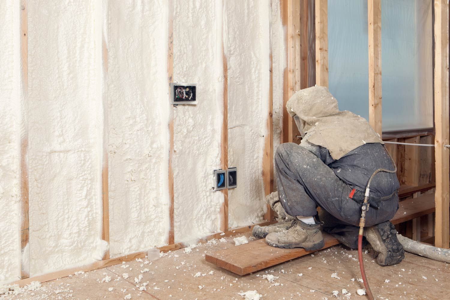 Person in protective suit spraying insulation into a wall cavity.