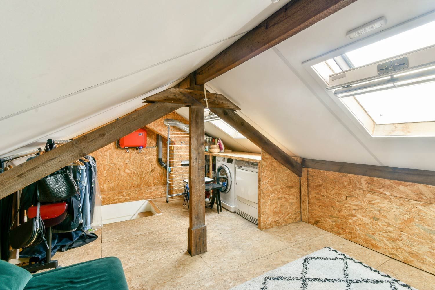 Attic room with exposed beams and chipboard walls. Includes a washing machine, clothes rack, and skylight.