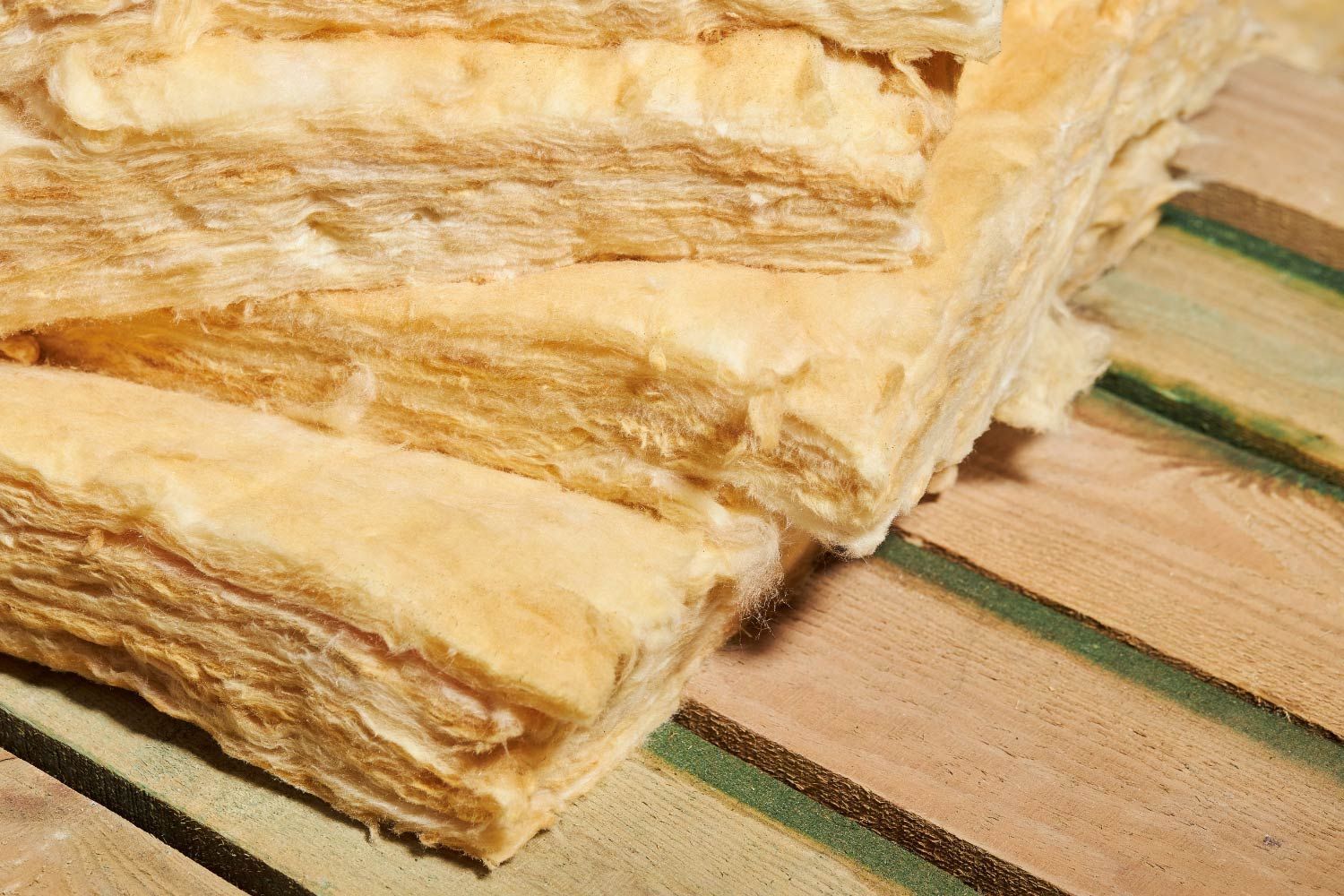 Close-up of stacked, batt insulation boards on a light-brown, striped wooden surface.