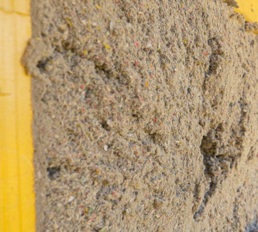 Close-up of cellulose insulation, gray and textured, applied to a yellow wooden surface.