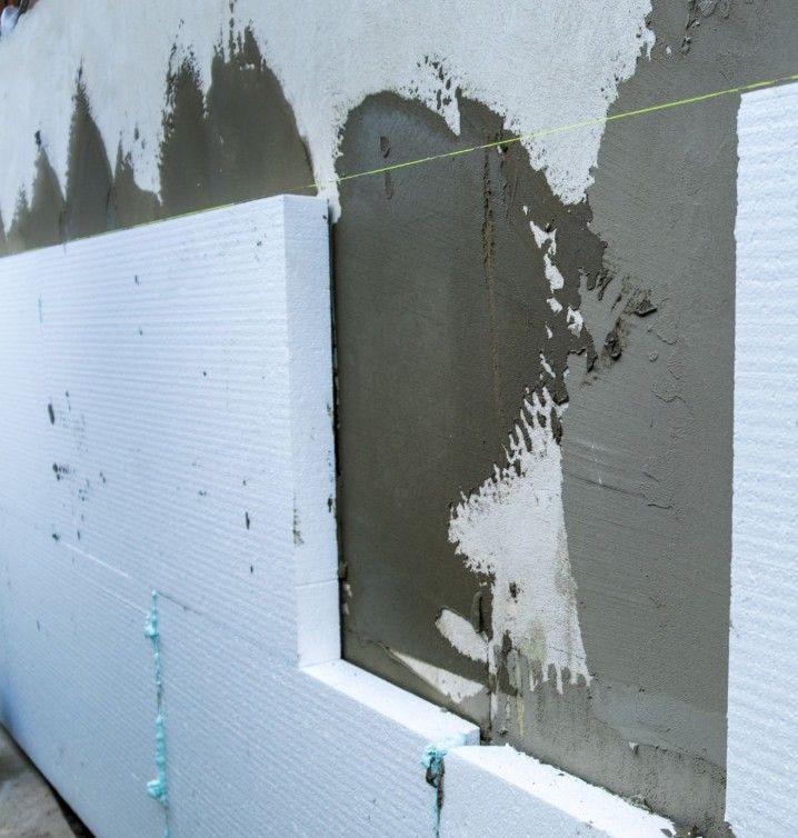 Person in protective gear sprays insulation into a wooden wall frame.