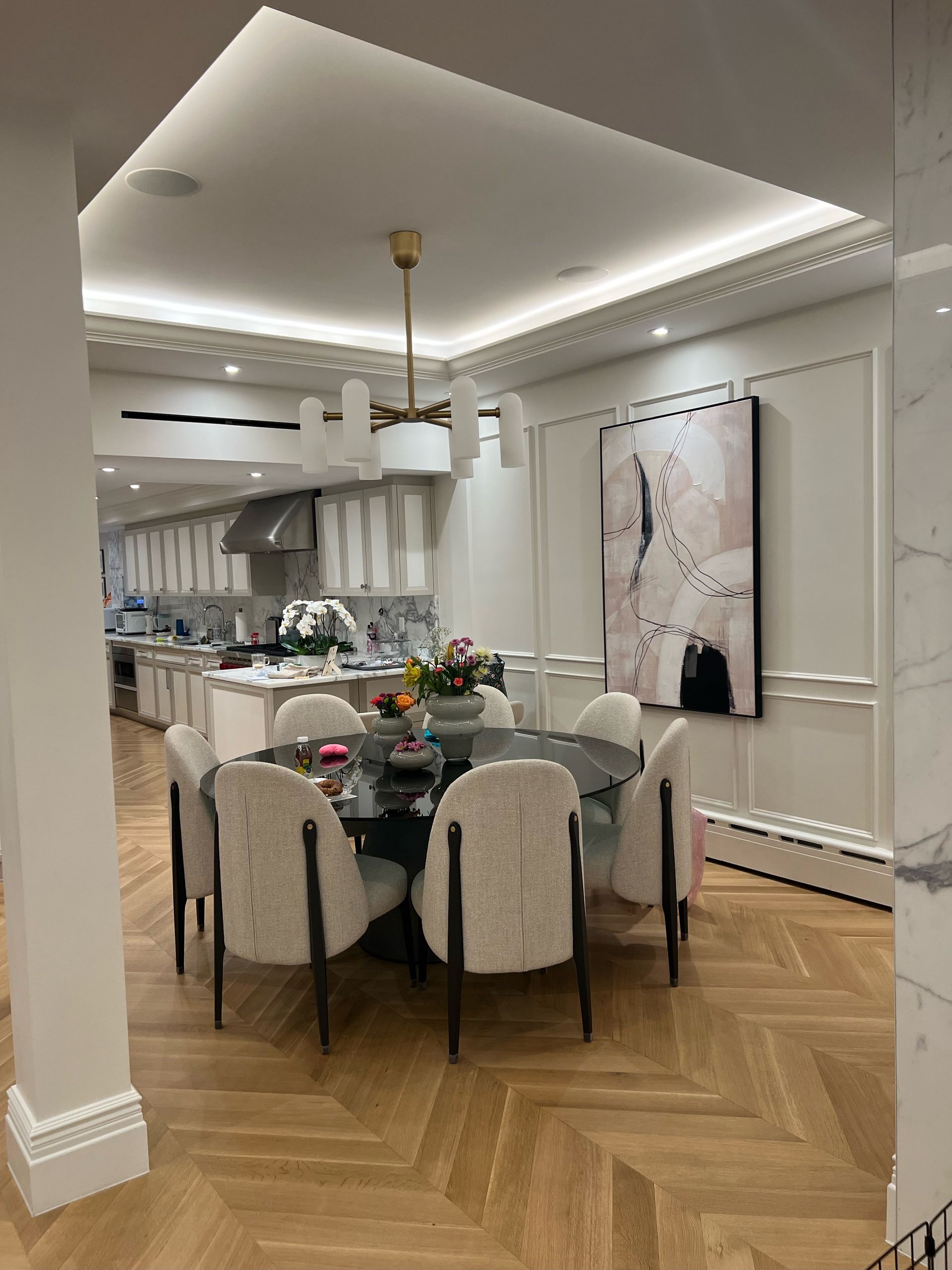 A dining room with a round table and chairs and a kitchen in the background.