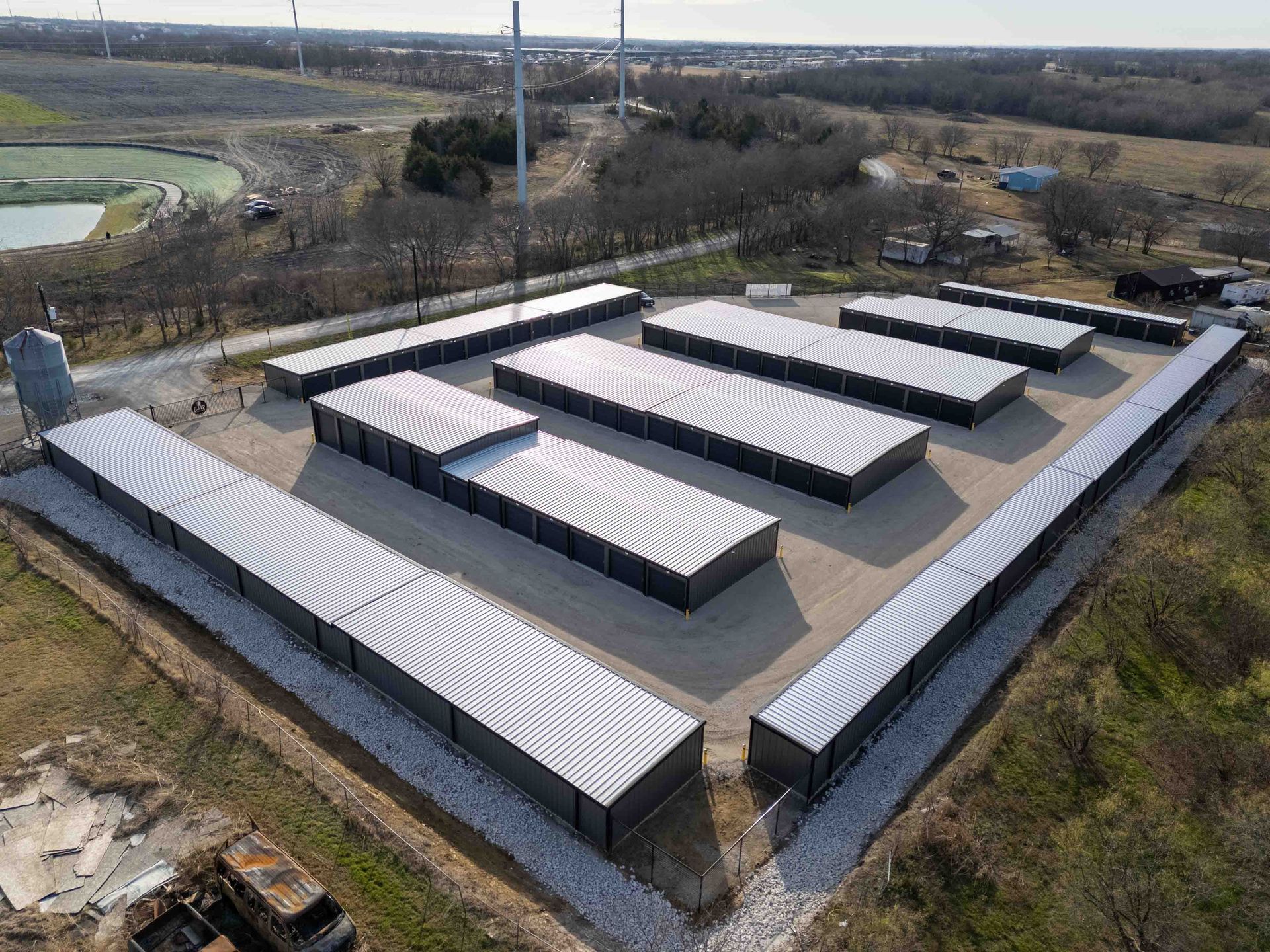 Aerial view of a rectangular arrangement of gray industrial buildings, possibly storage units, on a gravel lot.