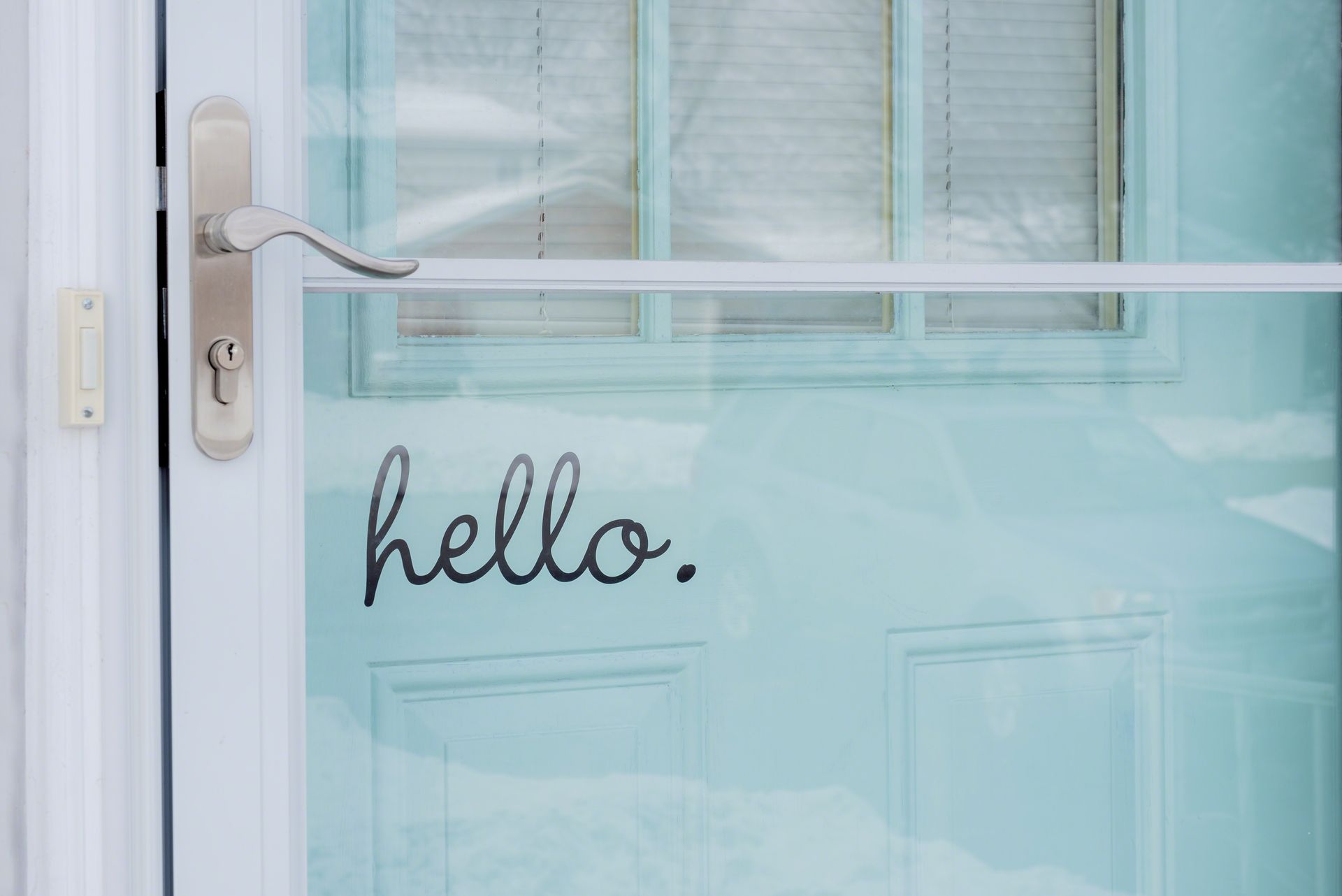 A front door with a storm door painted turquoise blue with the word hello.