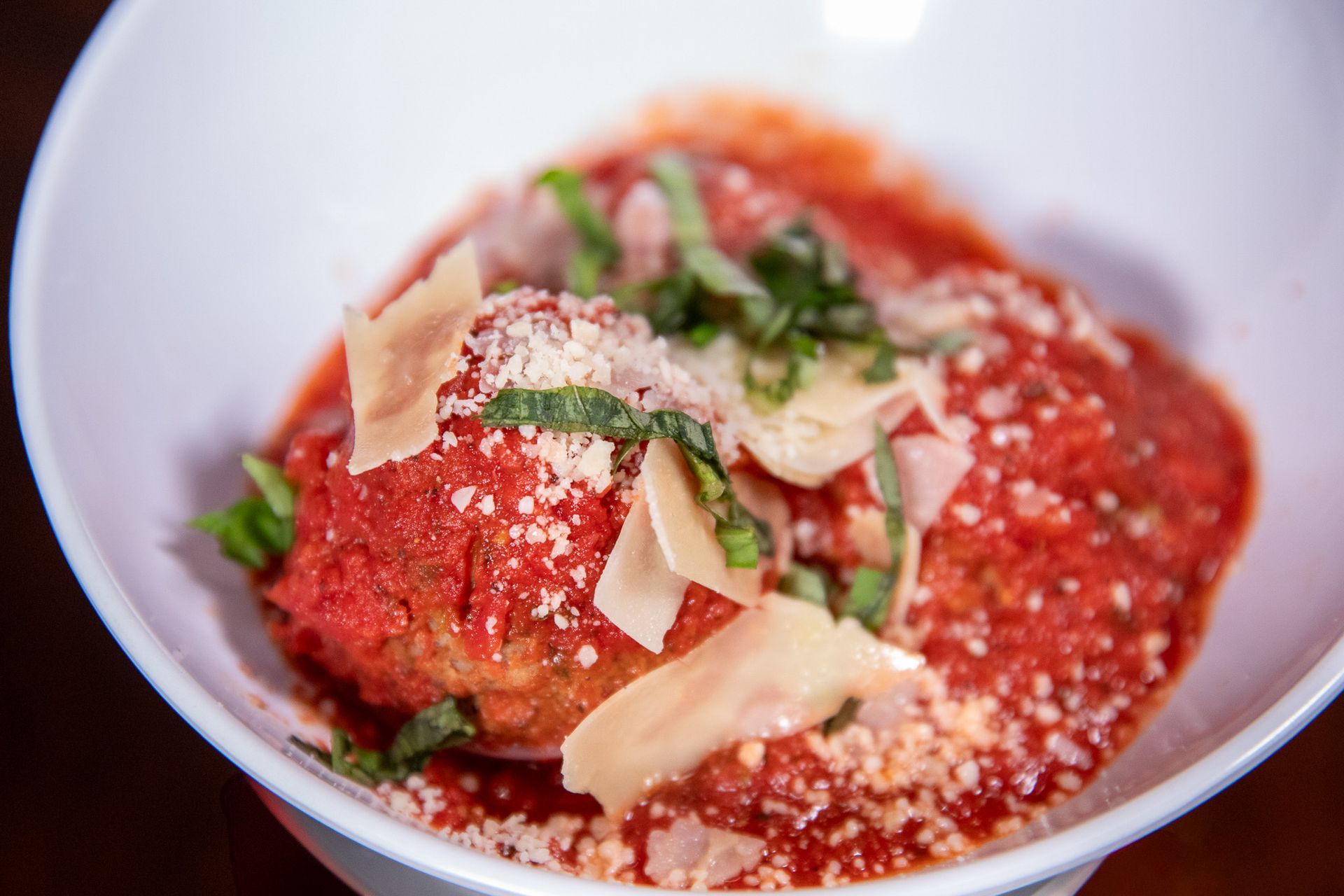 Meatballs in tomato sauce, garnished with basil and shaved parmesan in a white bowl.