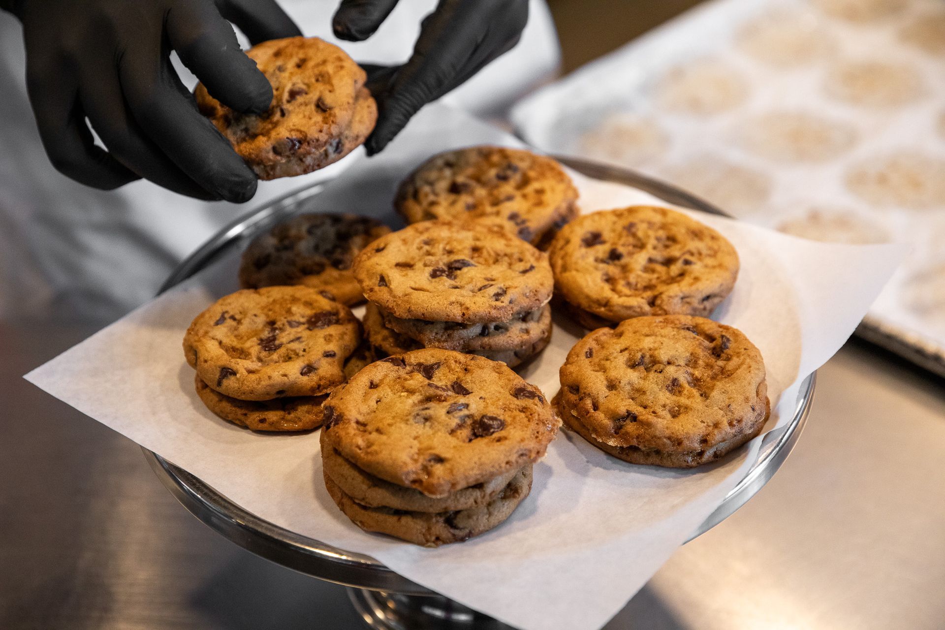 Person in black gloves arranging chocolate chip cookies on a serving platter.