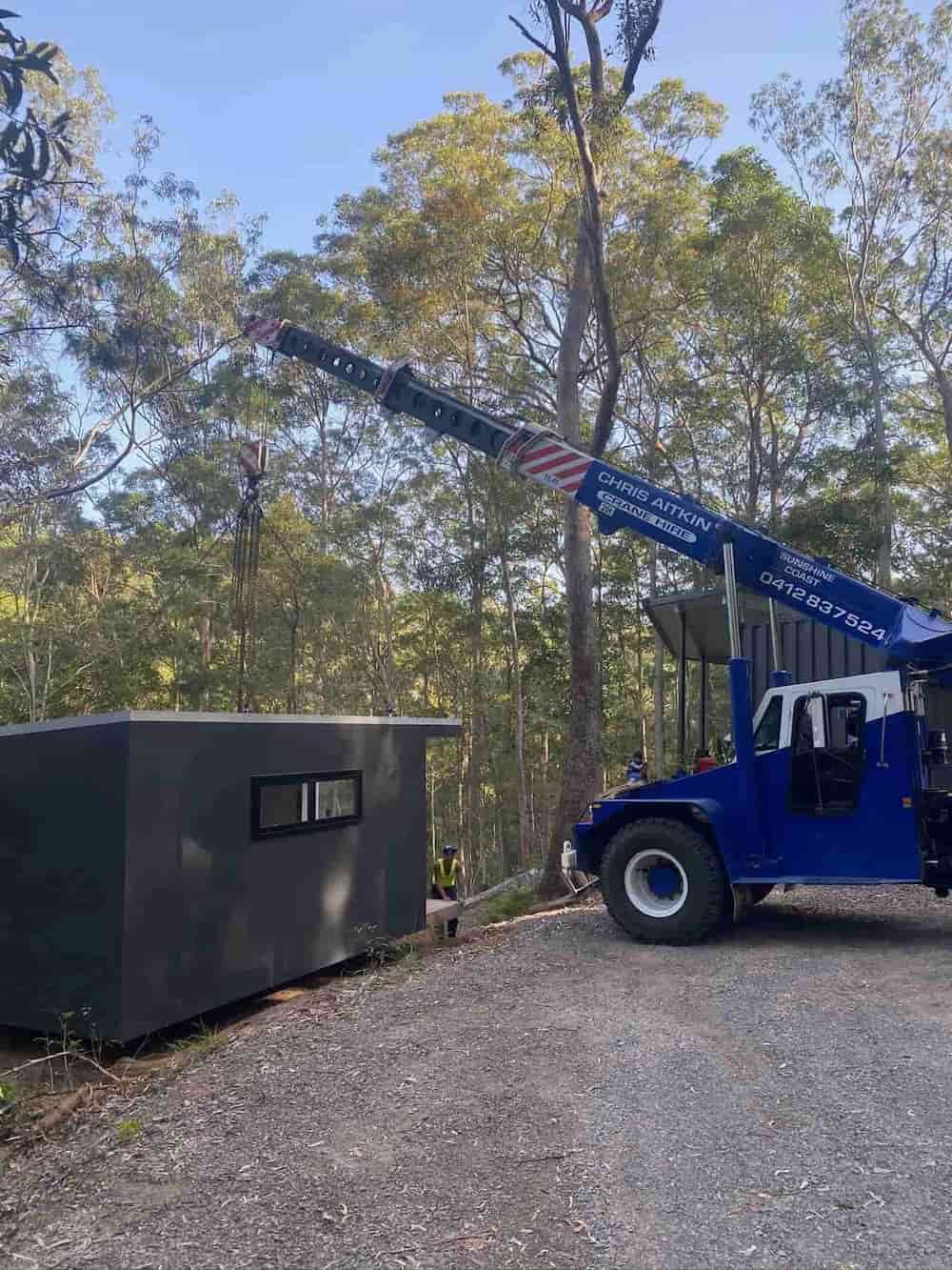 A Blue Truck With A Crane Attached To It Is Driving Down A Gravel Road — CA Crane Hire in Forest Glen, QLD