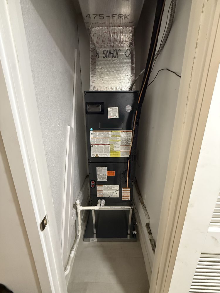 HVAC unit in a narrow utility closet, with ductwork and wiring visible. White walls and door frames.