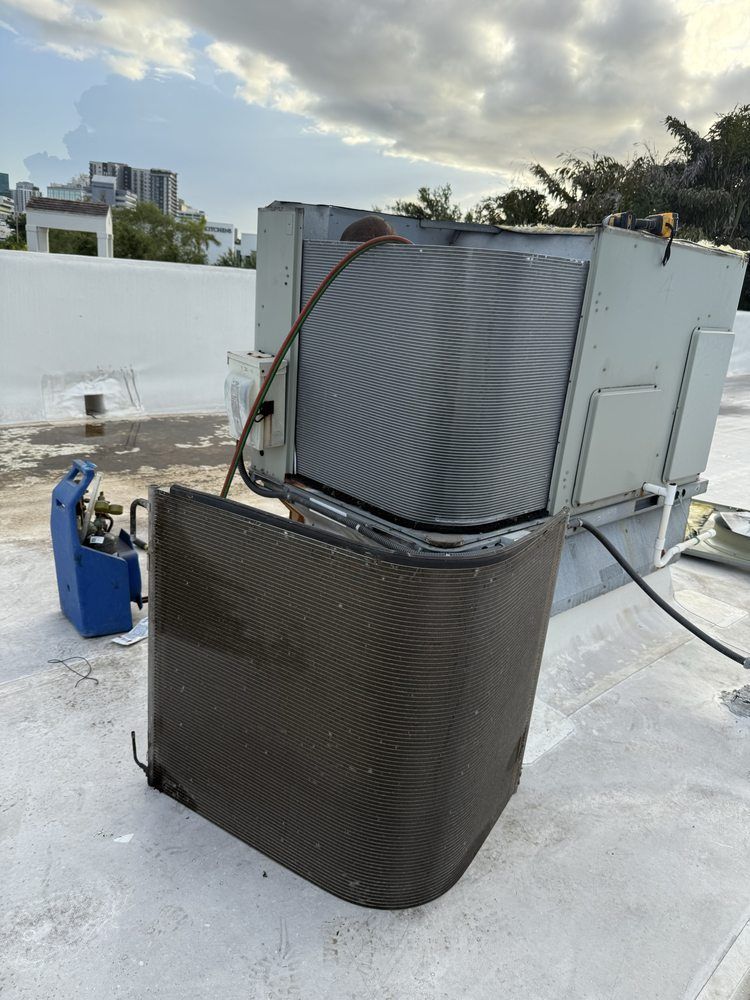 An air conditioning unit on a white rooftop, with detached coil and tools, cloudy sky background.