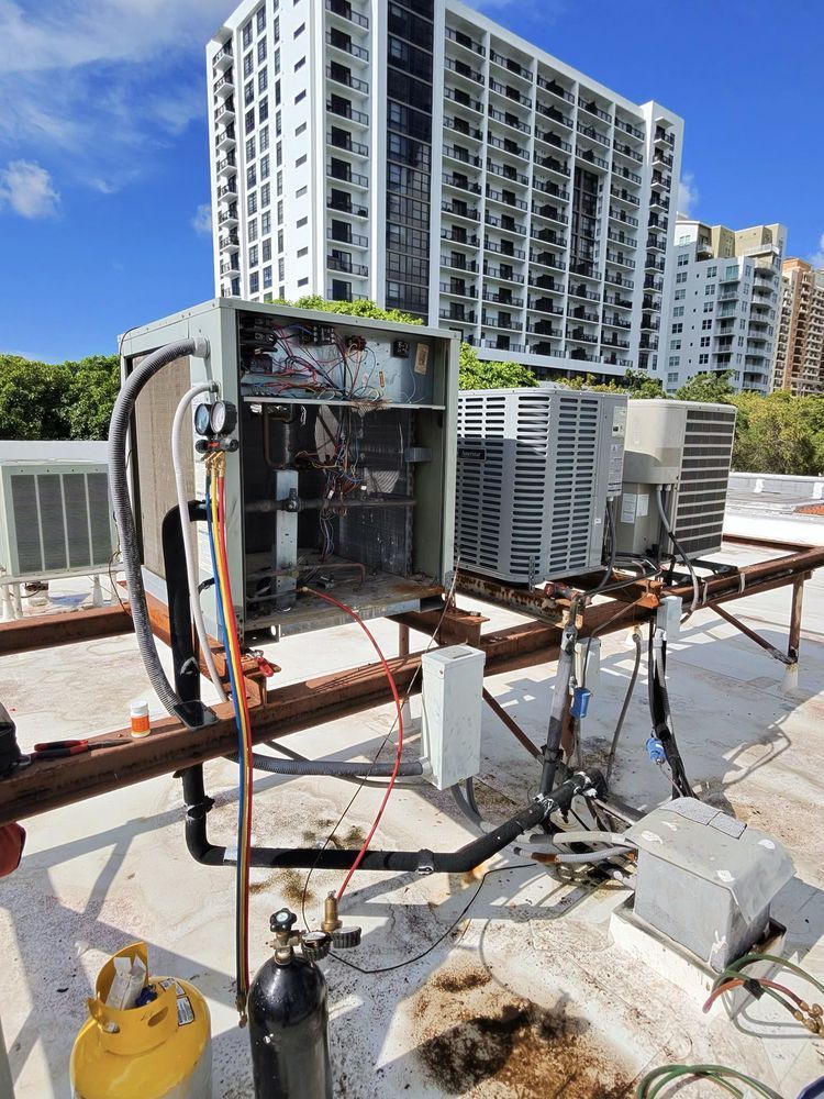 HVAC unit on a rooftop being serviced. Open electrical panel, multiple air conditioning units, and a welding torch.