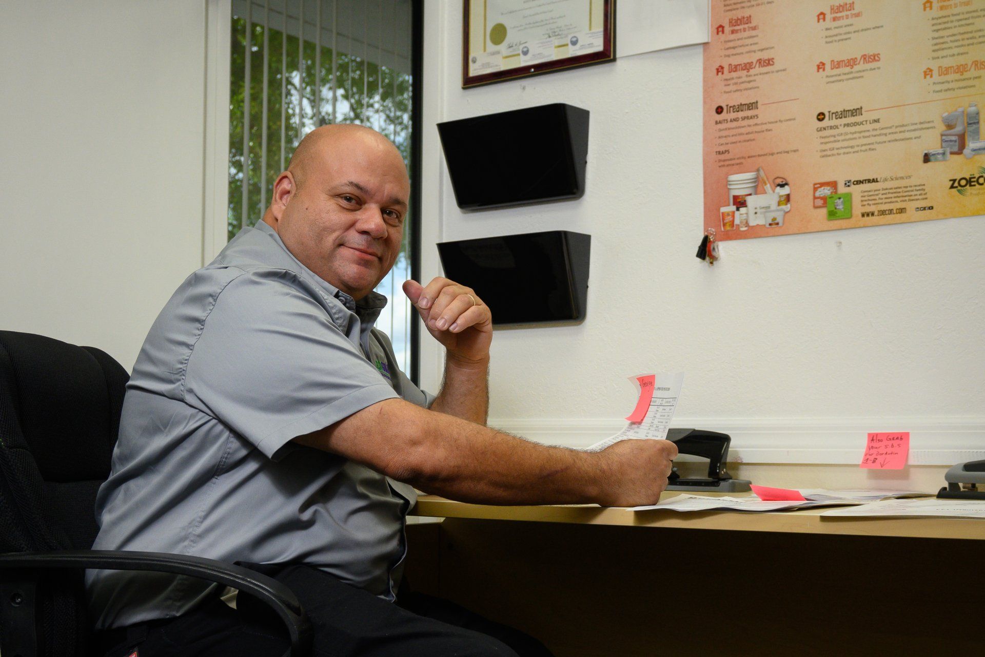 A man is sitting at a desk with a poster on the wall behind him.
