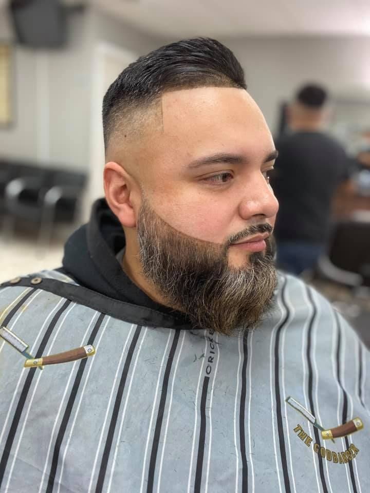 A man with a beard is getting his hair cut at a barber shop.