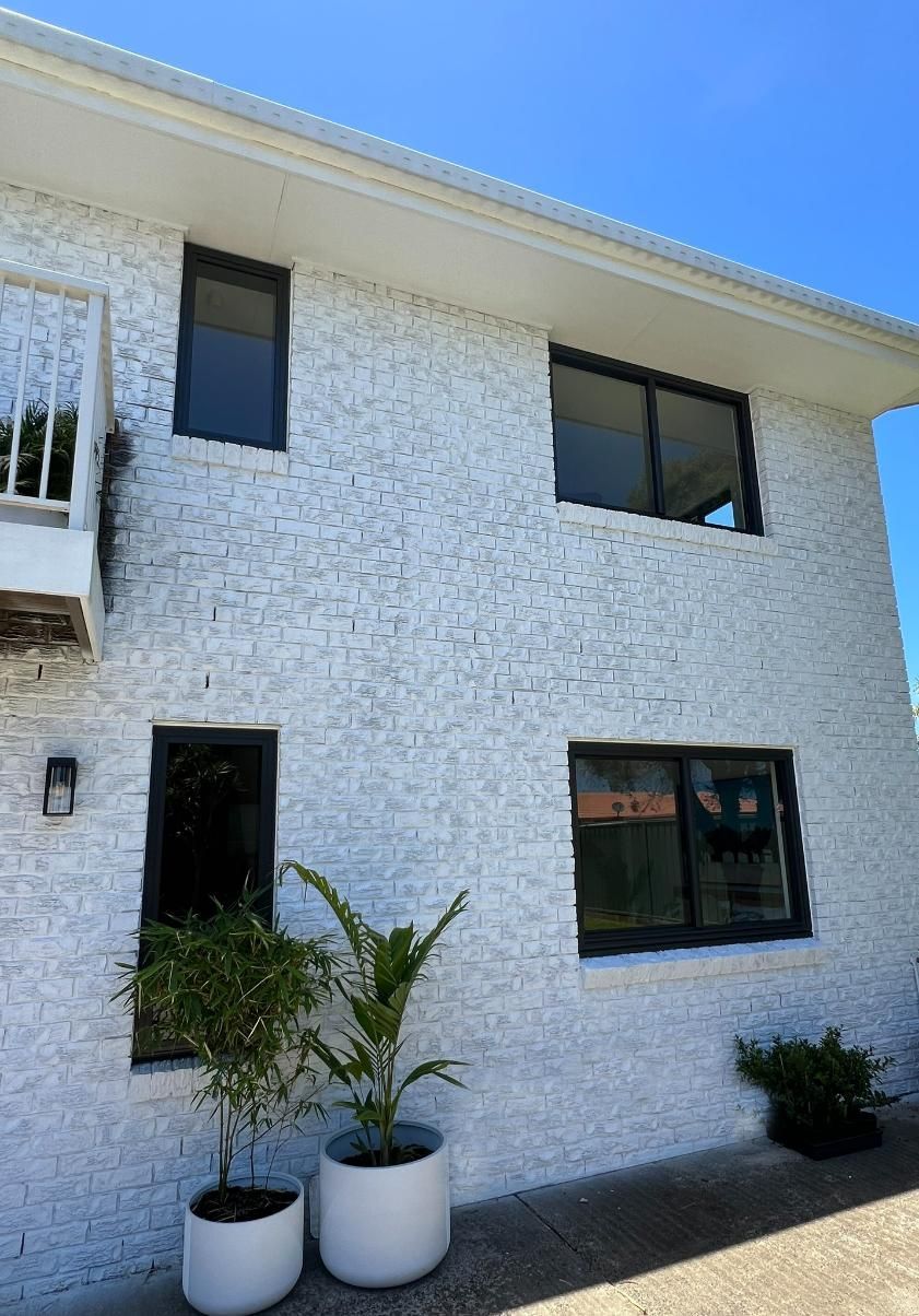 A White Brick Building With Two Potted Plants In Front Of It — Datco Windows & Doors Pty Ltd In Lismore, NSW
