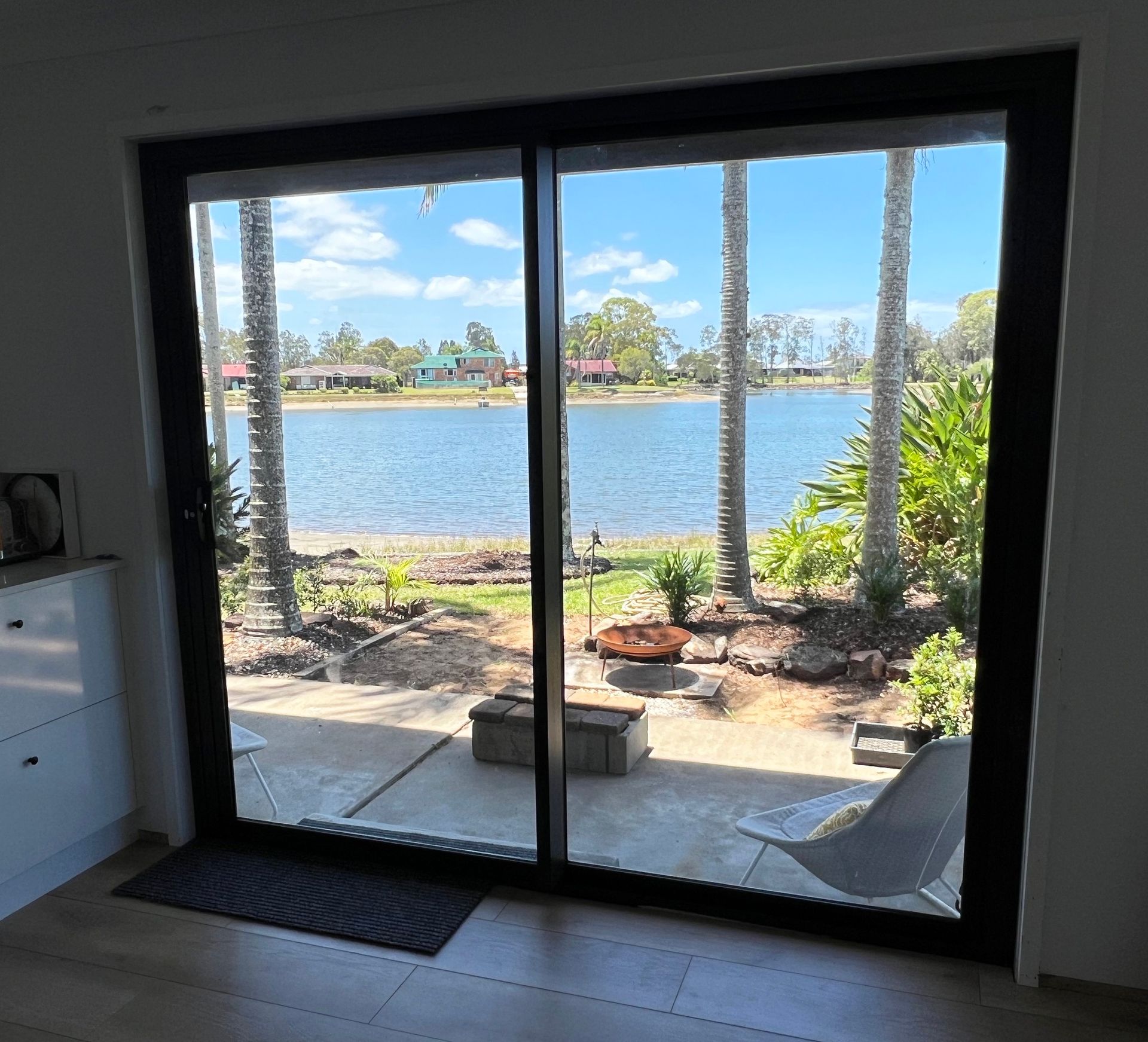 Sliding Glass Door Frames a Lake View With Palm Trees — Datco Windows & Doors Pty Ltd In South Murwillumbah, NSW