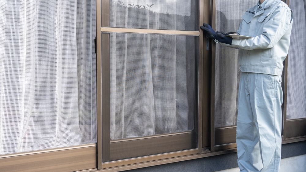 A Man Is Standing In Front Of A Window With A Screen On It — Datco Windows & Doors Pty Ltd In Casino, NSW