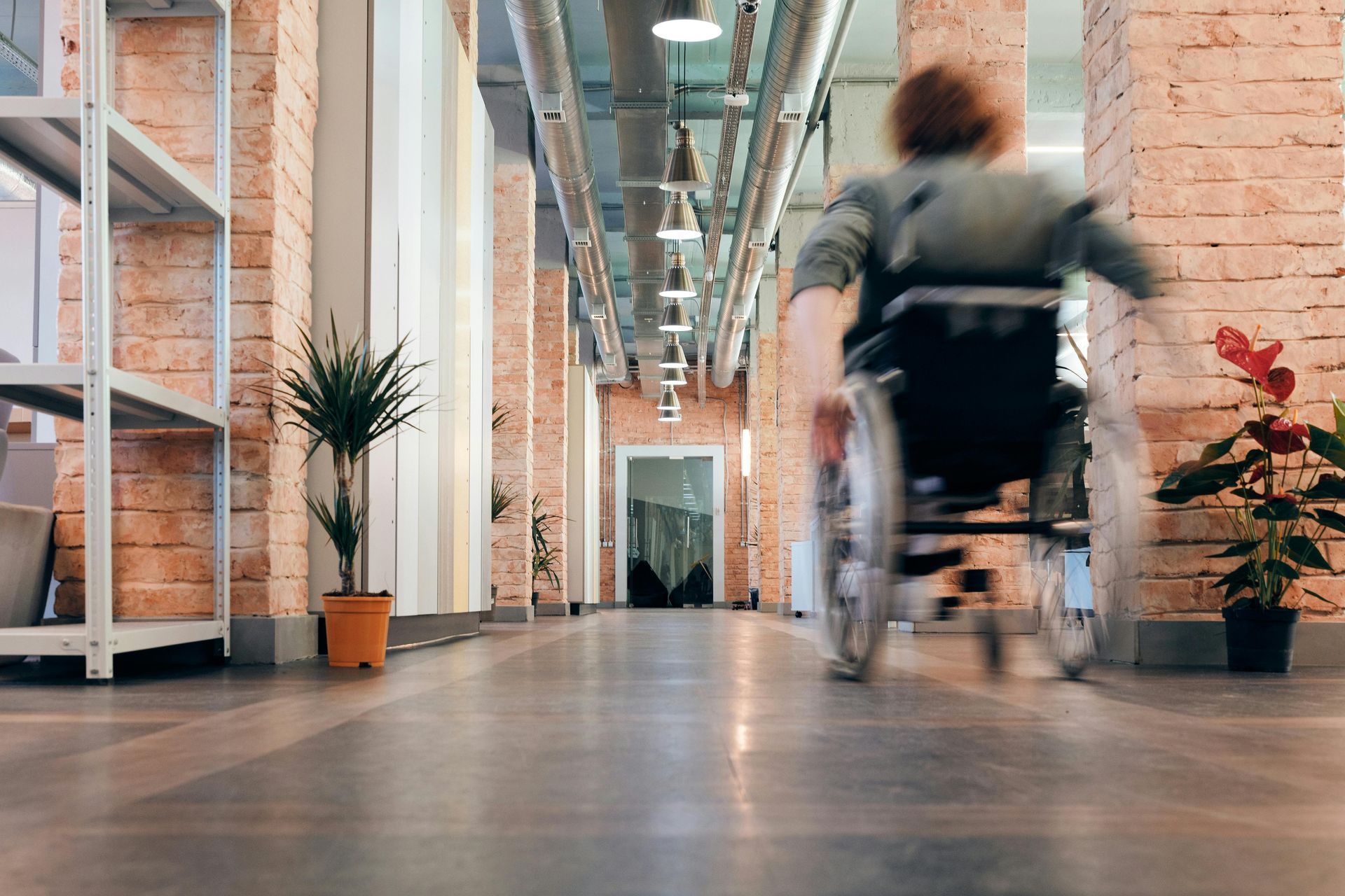 Person in wheelchair moving quickly down an office hallway, blurred motion.