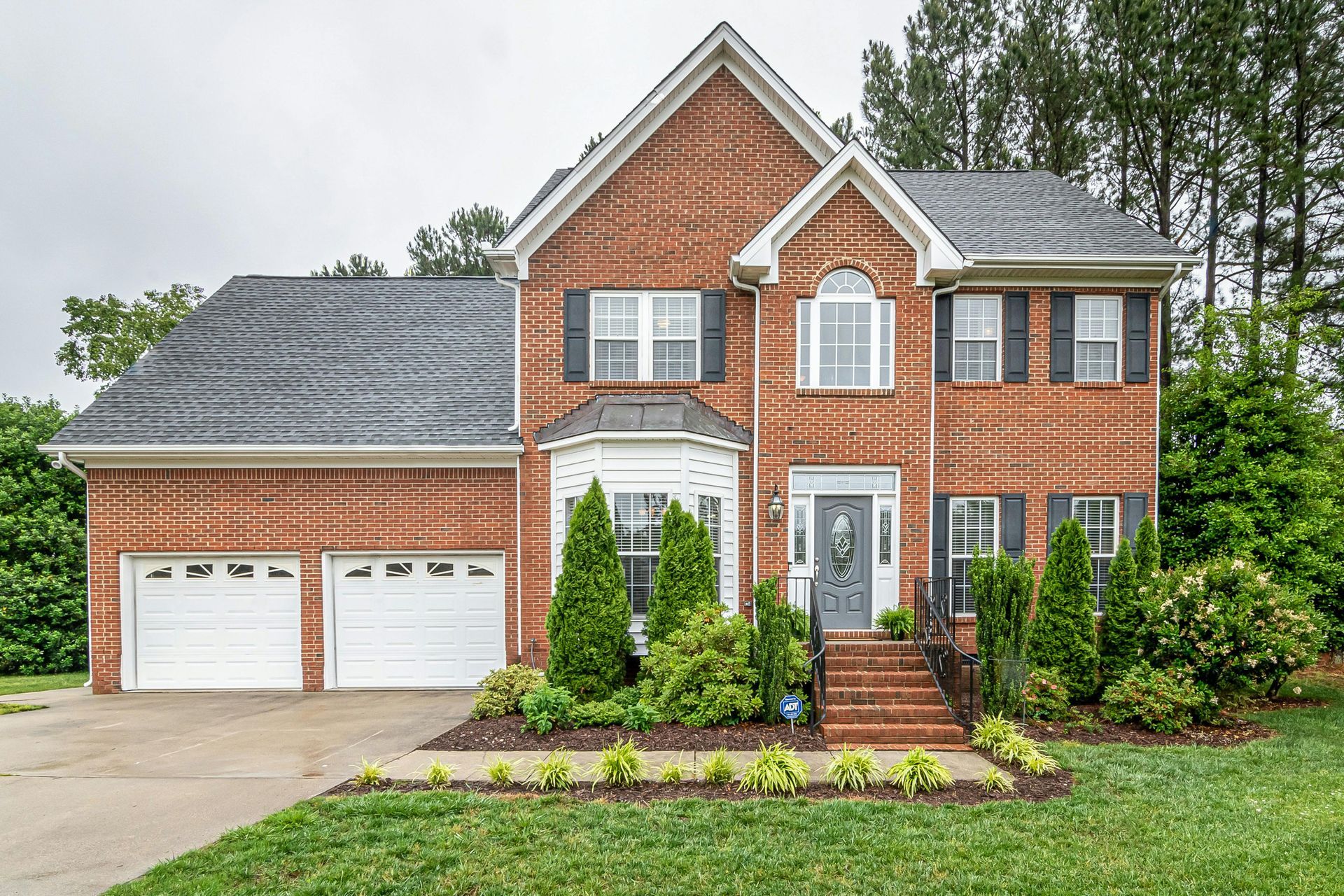 Brick two-story house with a two-car garage, black shutters, and a well-manicured lawn.