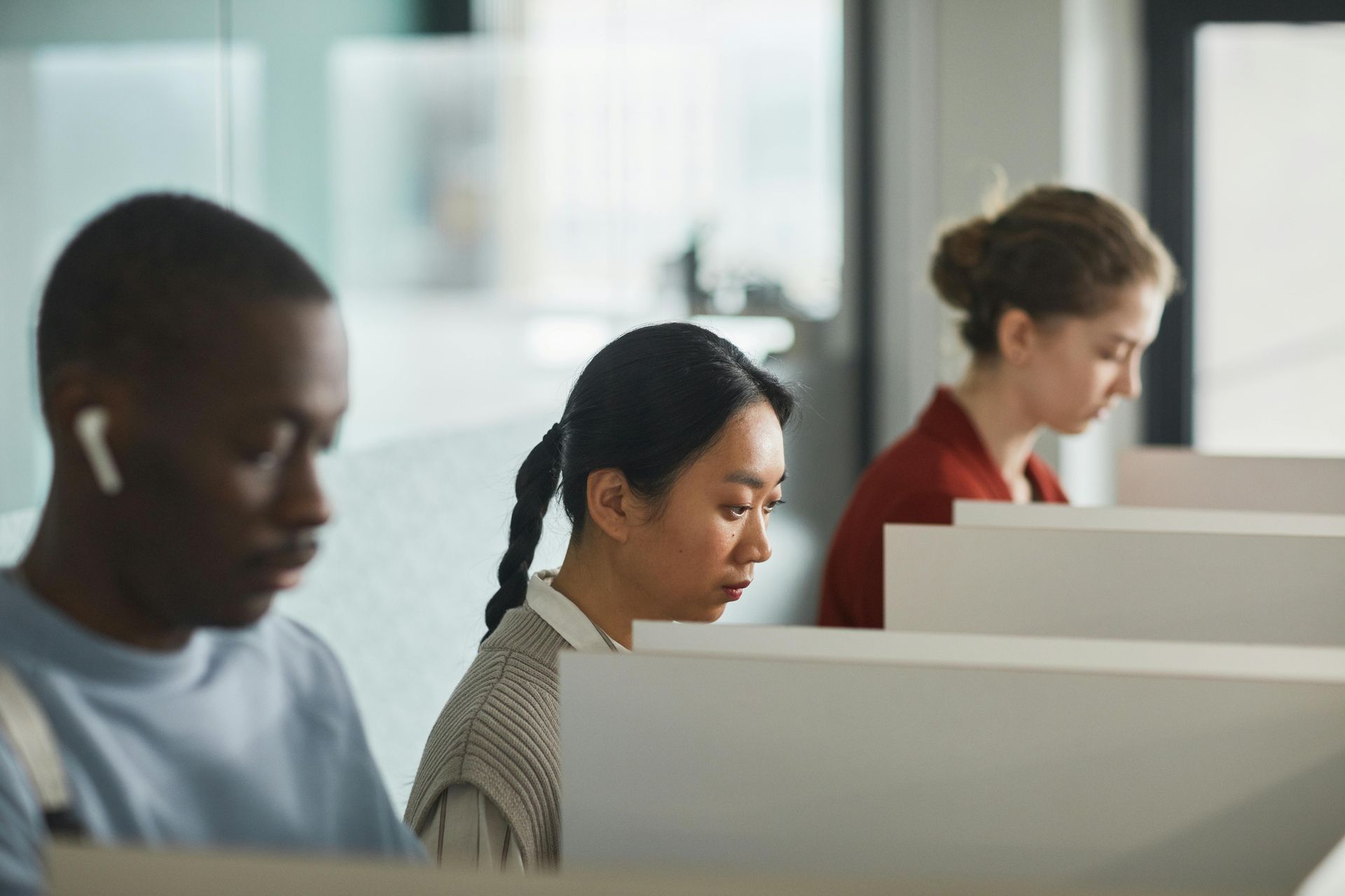 People working at desks in a brightly lit office. One person has earbuds.
