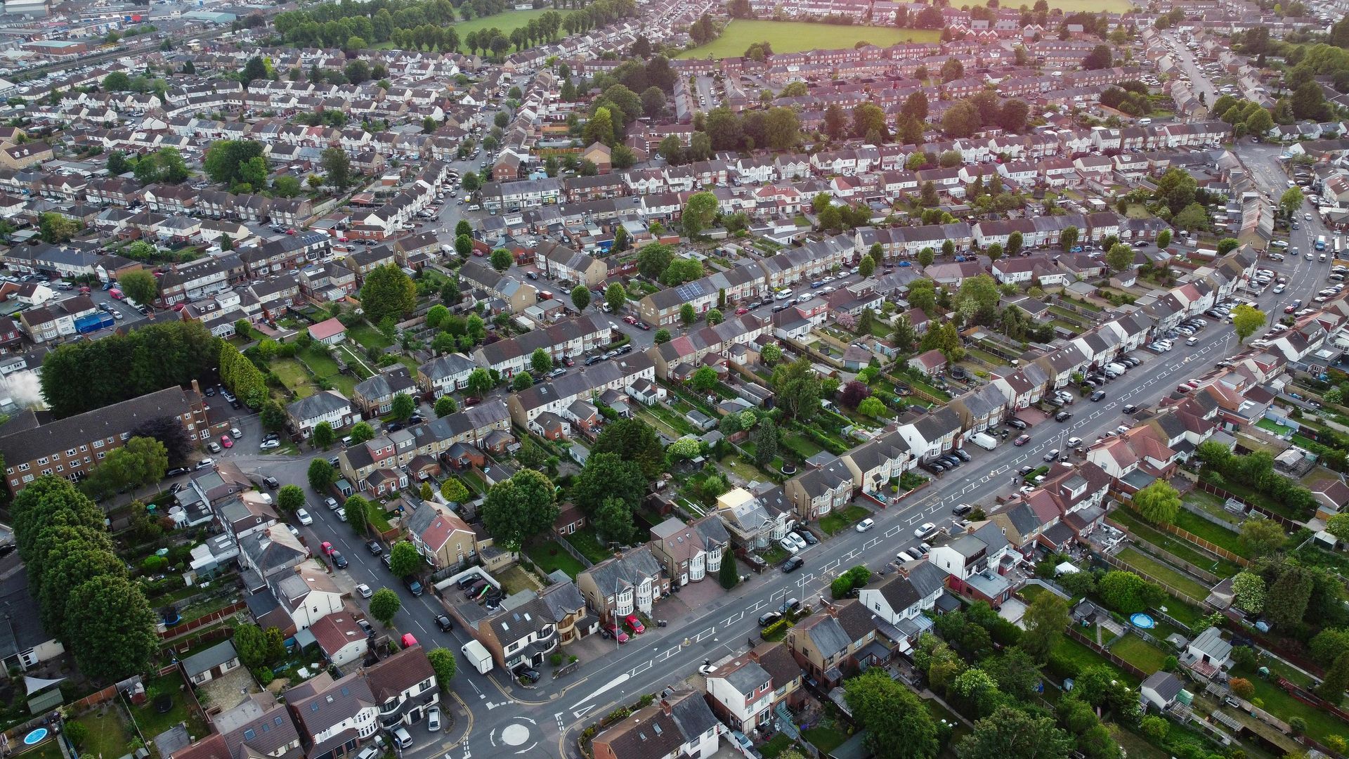 Aerial view of a suburban neighborhood with houses, roads, and trees under a cloudy sky.