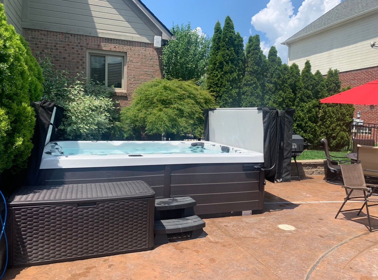 Backyard above-ground pool with hot tub, patio furniture, and red umbrella on a sunny day