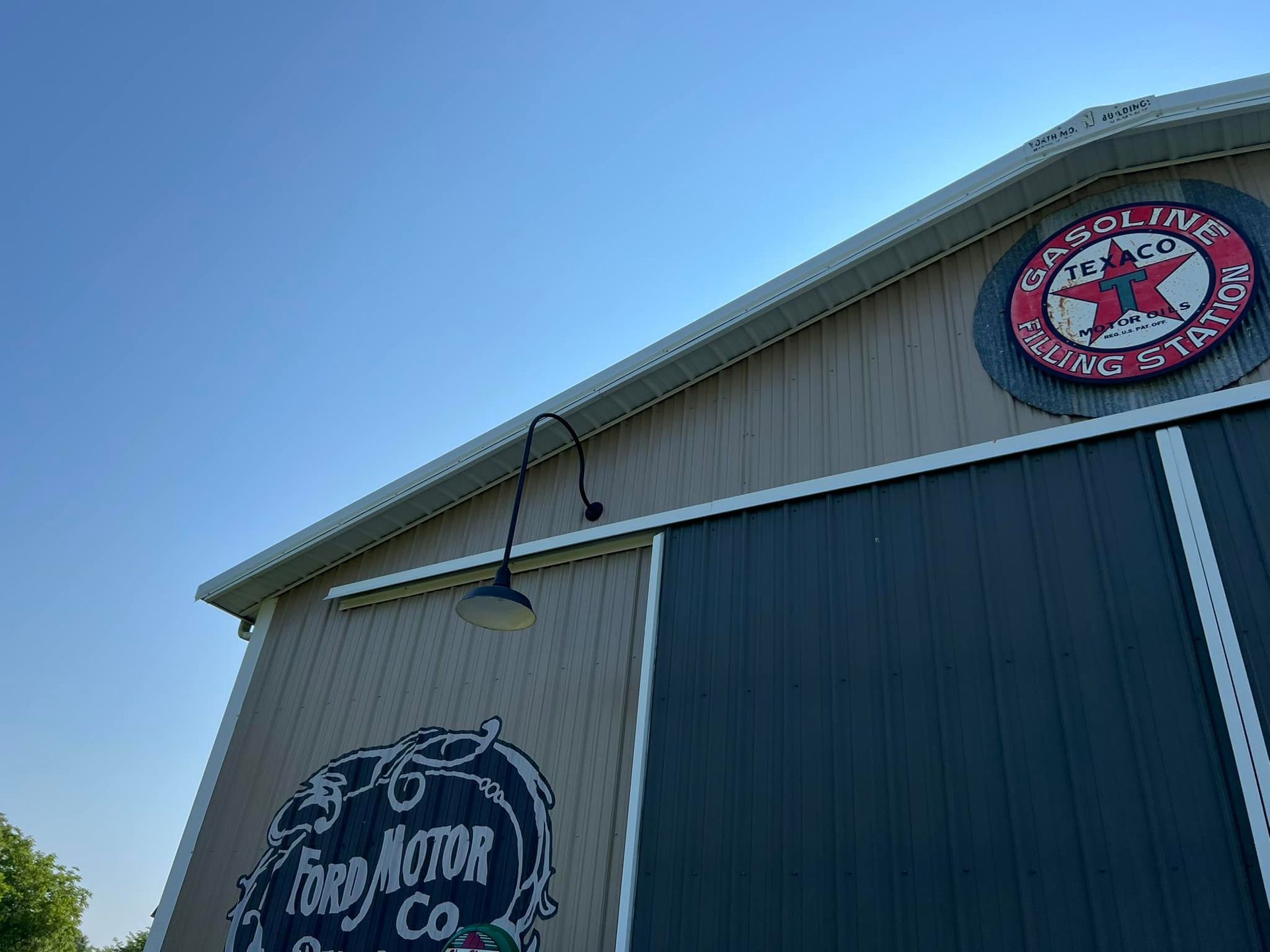 Barn with vintage gas station and Ford Motor Co. signs, blue door, and arched light against a blue sky.