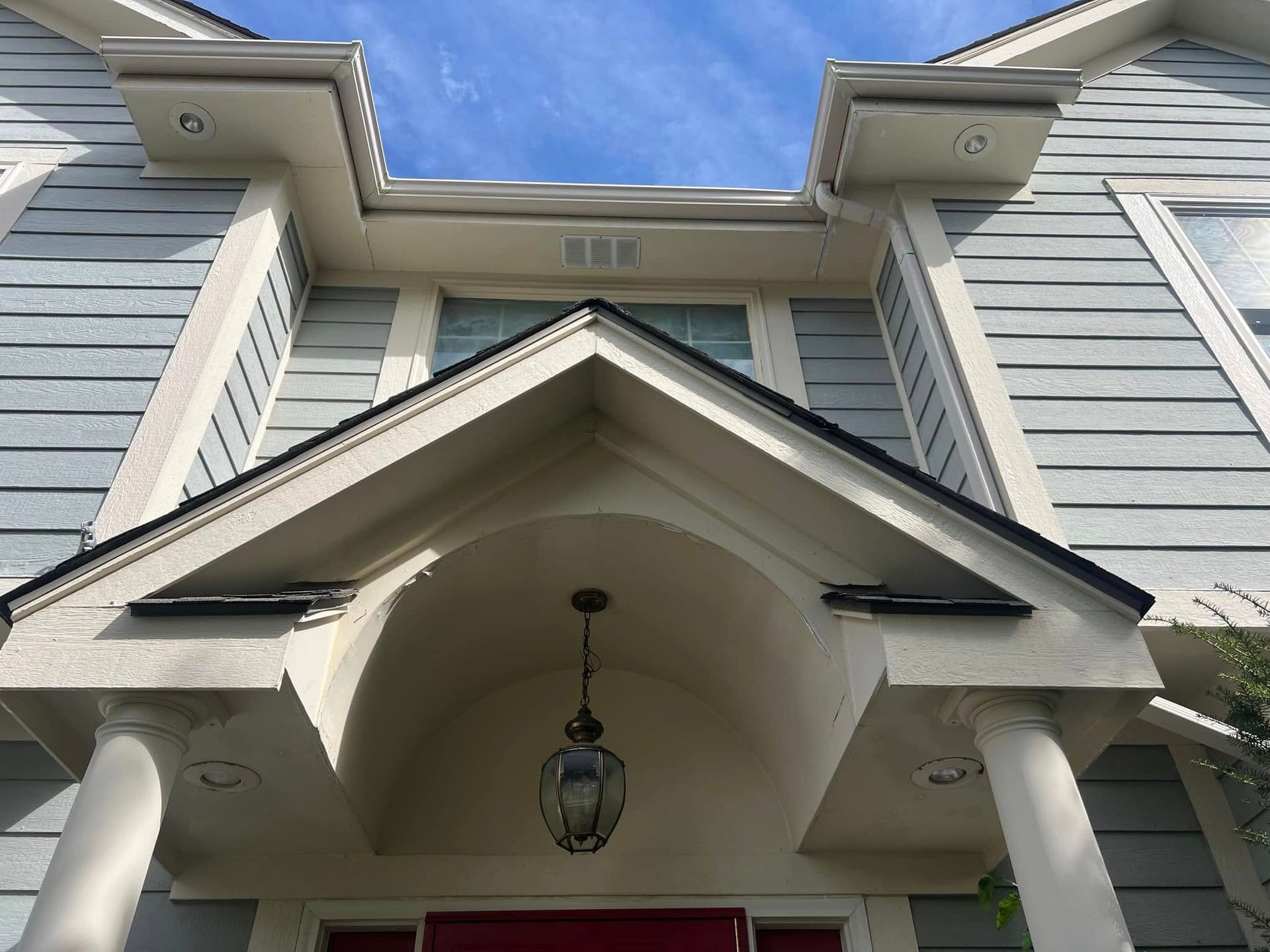 Exterior of a two-story home with light blue siding. Front entrance features an arched portico and a hanging light fixture.