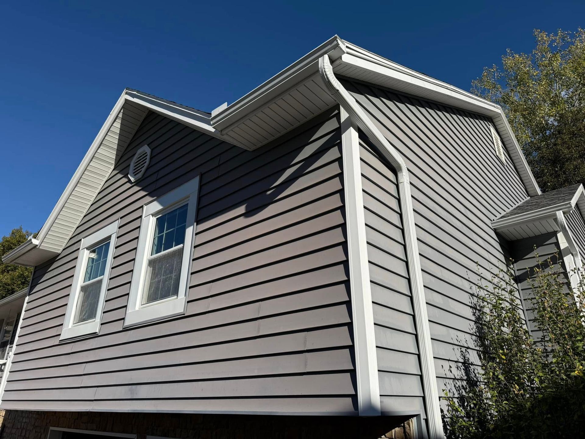 Gray sided house with white trim, gutters, and windows against a blue sky.