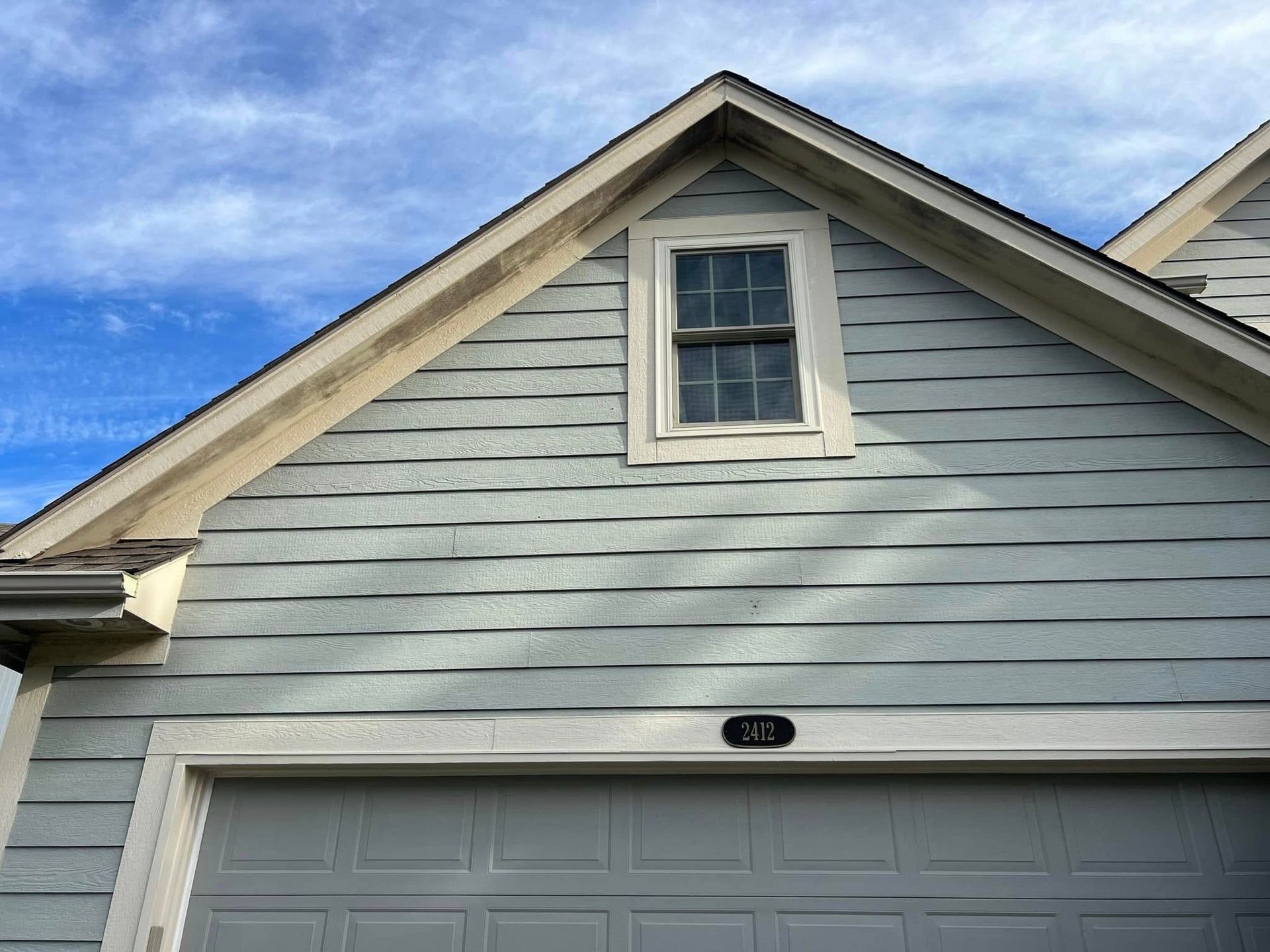 Light blue house exterior with a garage and a window under the roof peak.