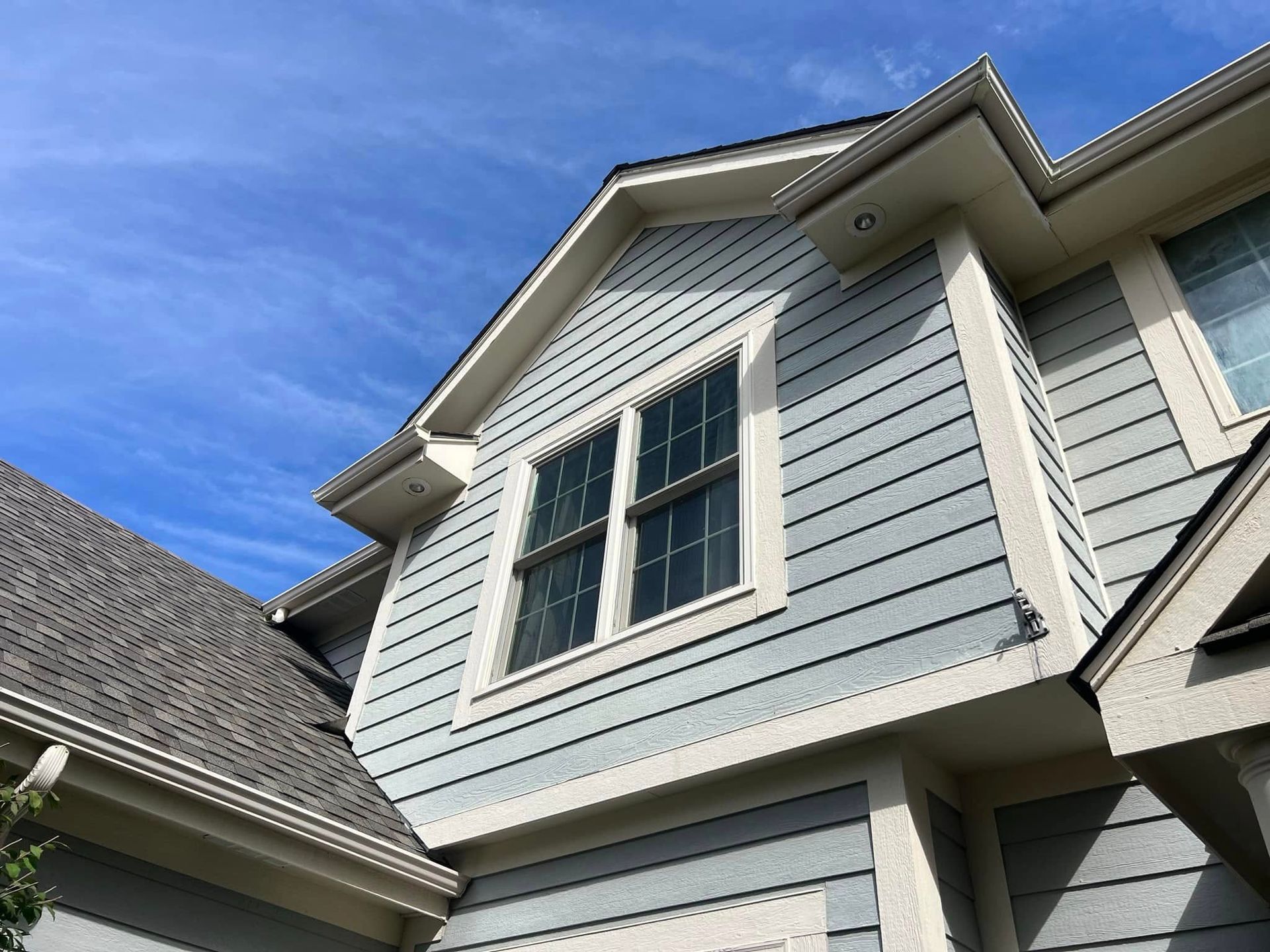 Light blue siding on a house with white trim, gray roof, and a bright blue sky.