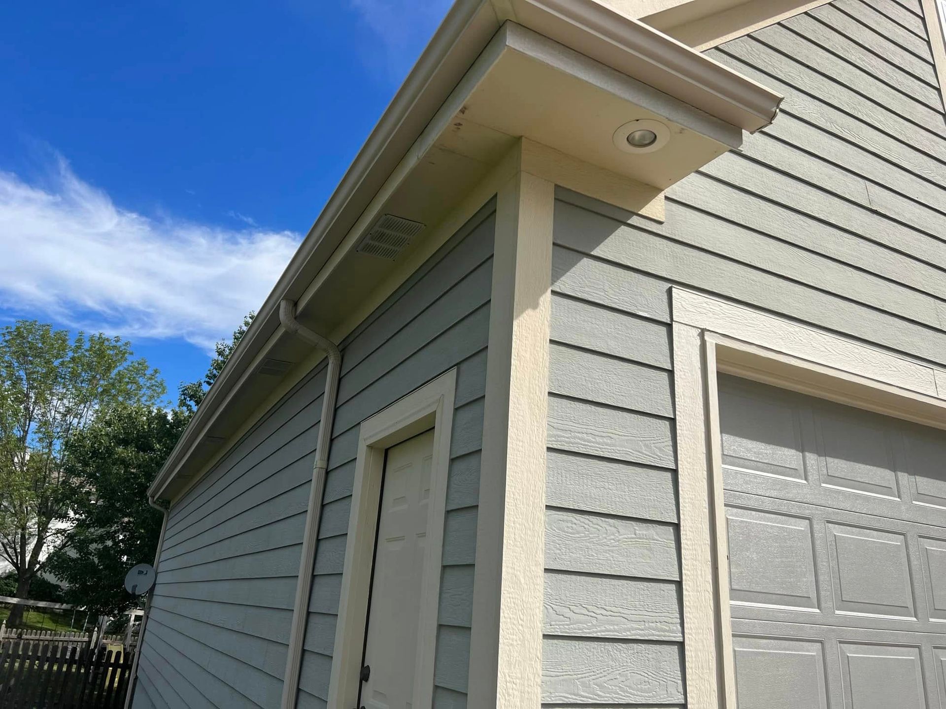 Light blue siding on a house with beige trim, a garage door, and a door on a sunny day.