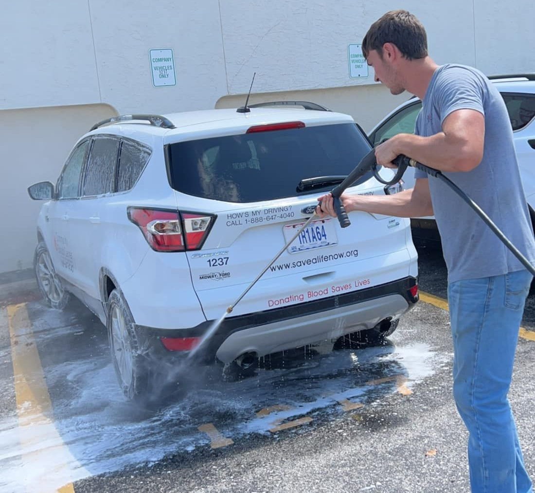 Man washing a white SUV in a parking space with a pressure washer.