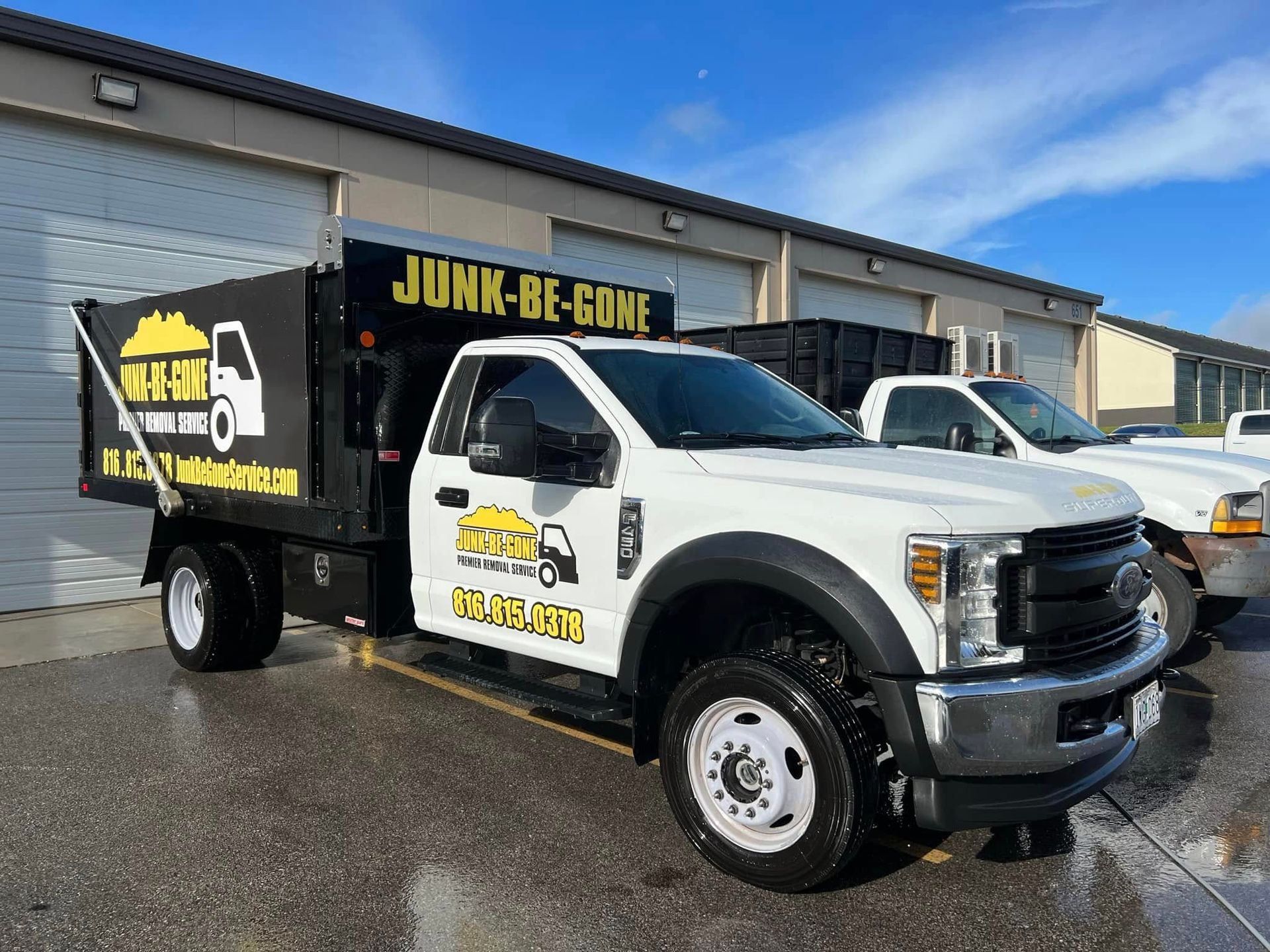 White Junk-Be-Gone truck parked in front of buildings on a bright day. Truck bed is black, and the company logo is visible.