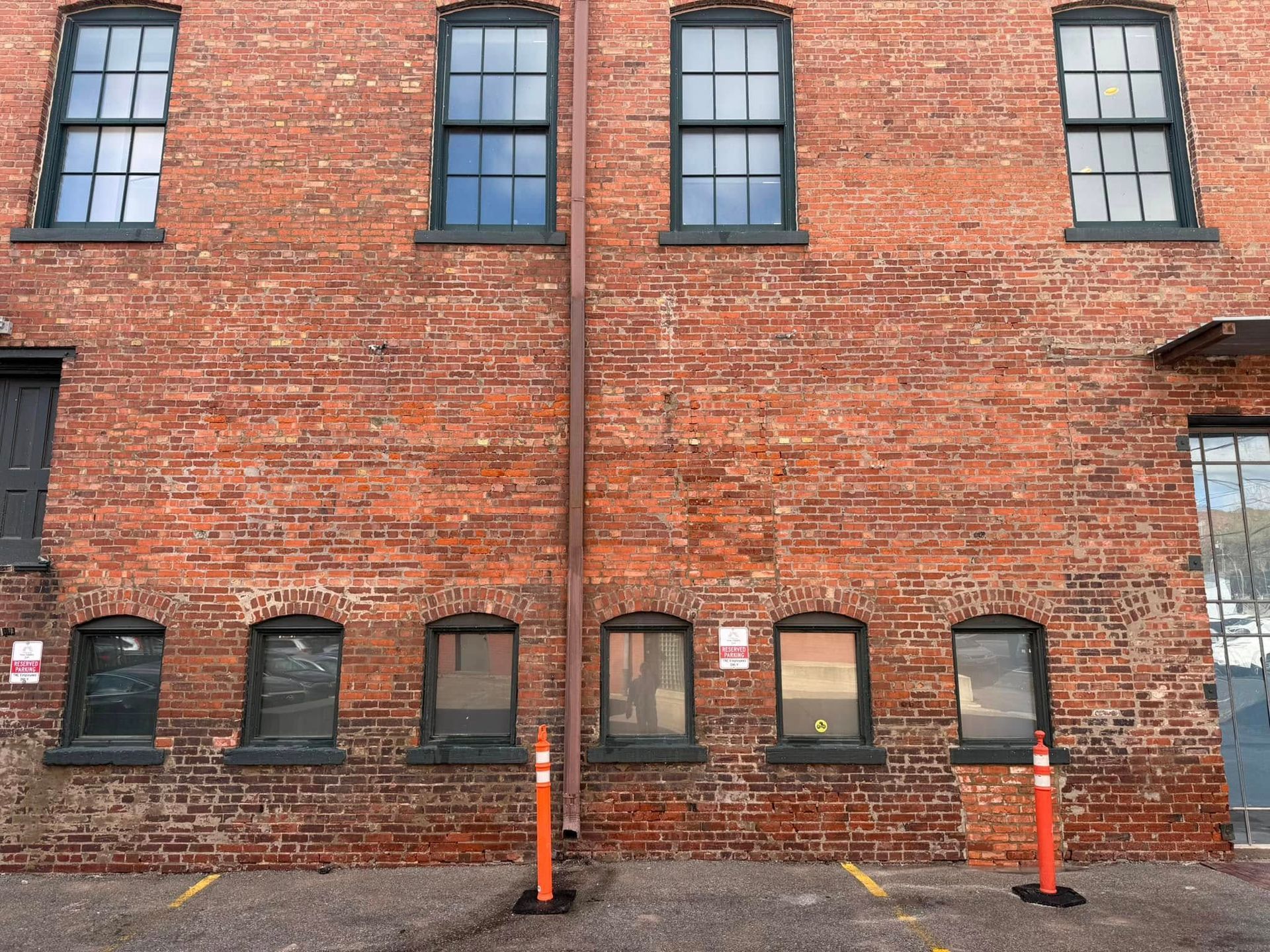 Red brick building with rows of windows and orange bollards.