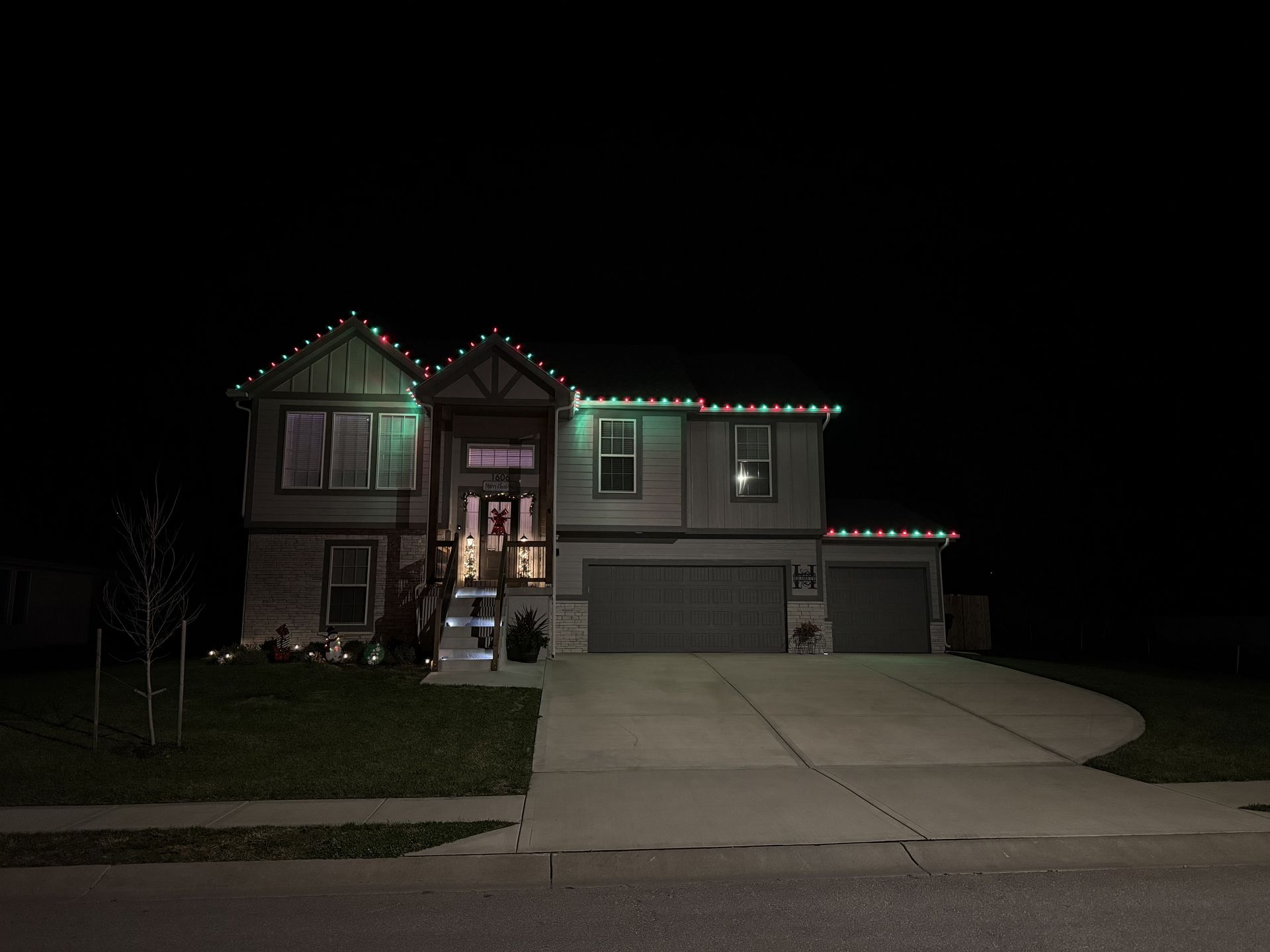 House at night decorated with green and white lights. Concrete driveway and garage.