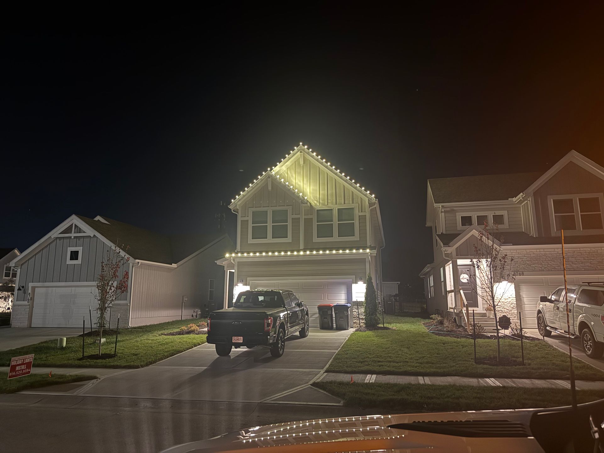 Suburban homes at night, one with Christmas lights around the roof. A truck is parked in the driveway.