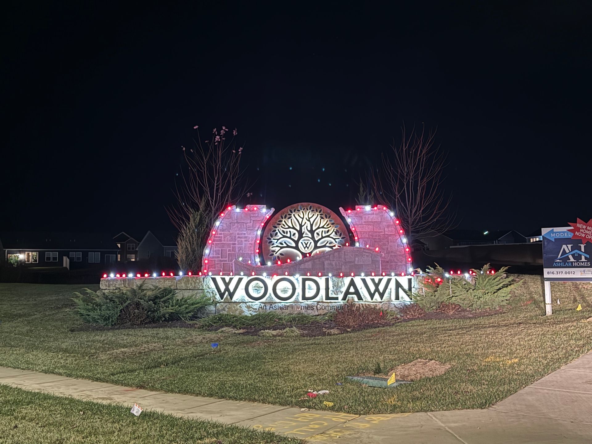 Woodlawn neighborhood sign lit with Christmas lights at night.