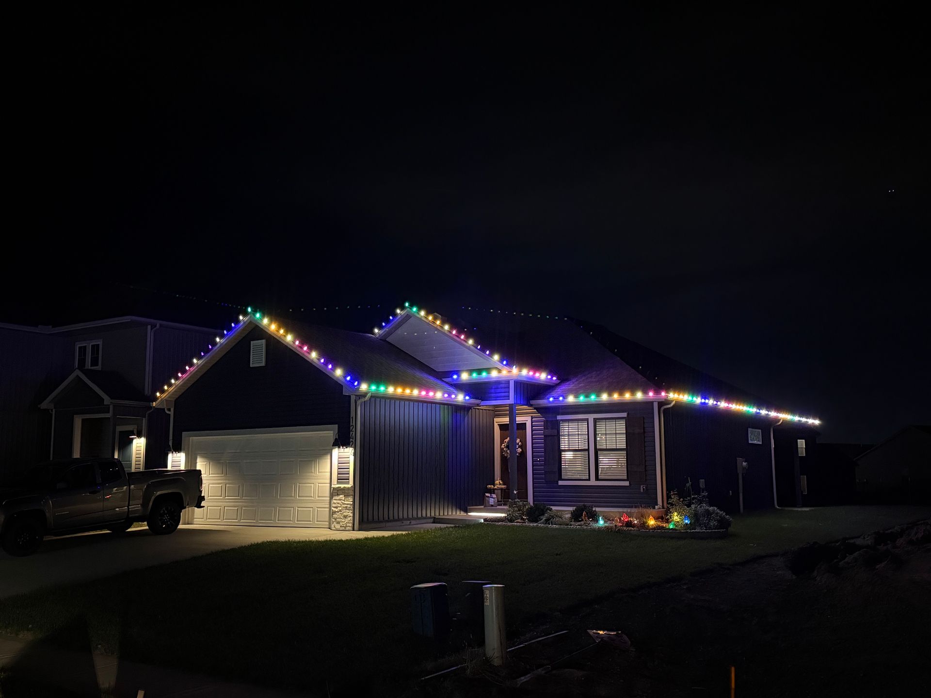 House at night with roofline illuminated by colorful Christmas lights.