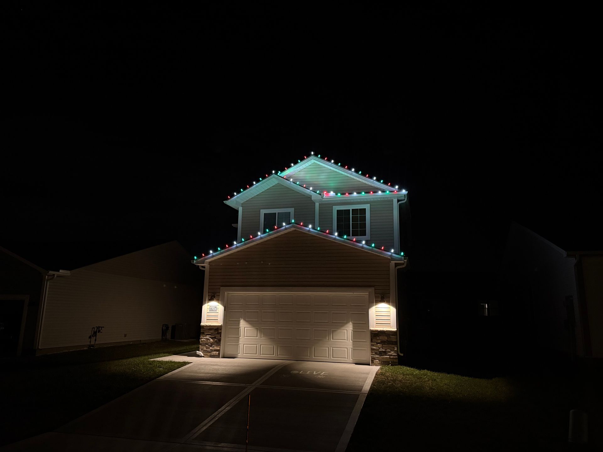 Two-story house with green, red, and white Christmas lights along the roof at night.