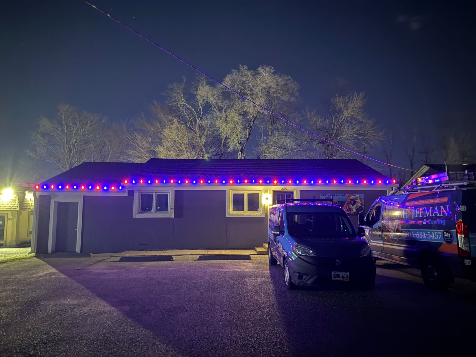 A building with blue and red Christmas lights on its roof at night, with a parked van in front.