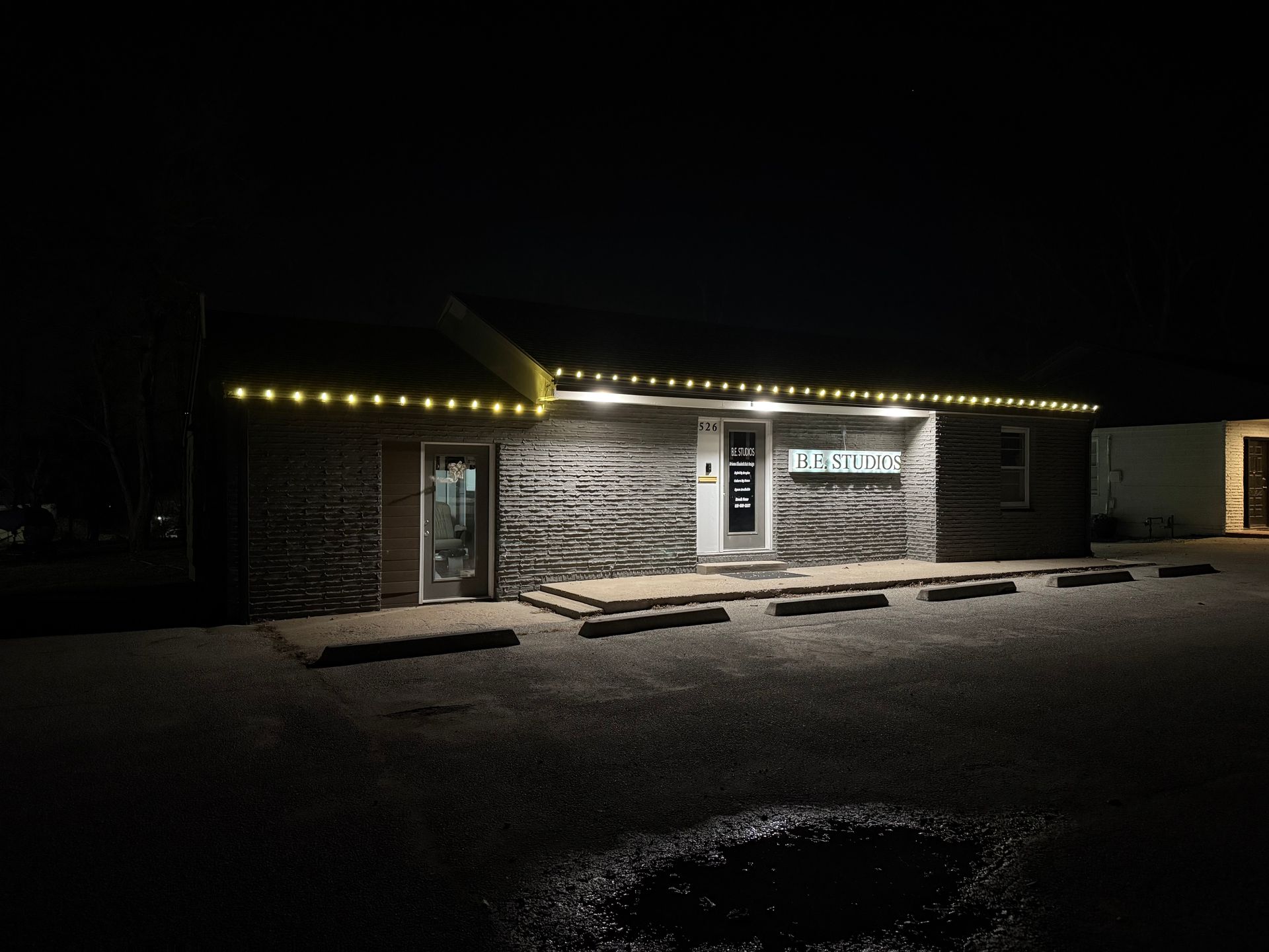 A building with string lights at night. The facade is stone-like. There's a door and windows.