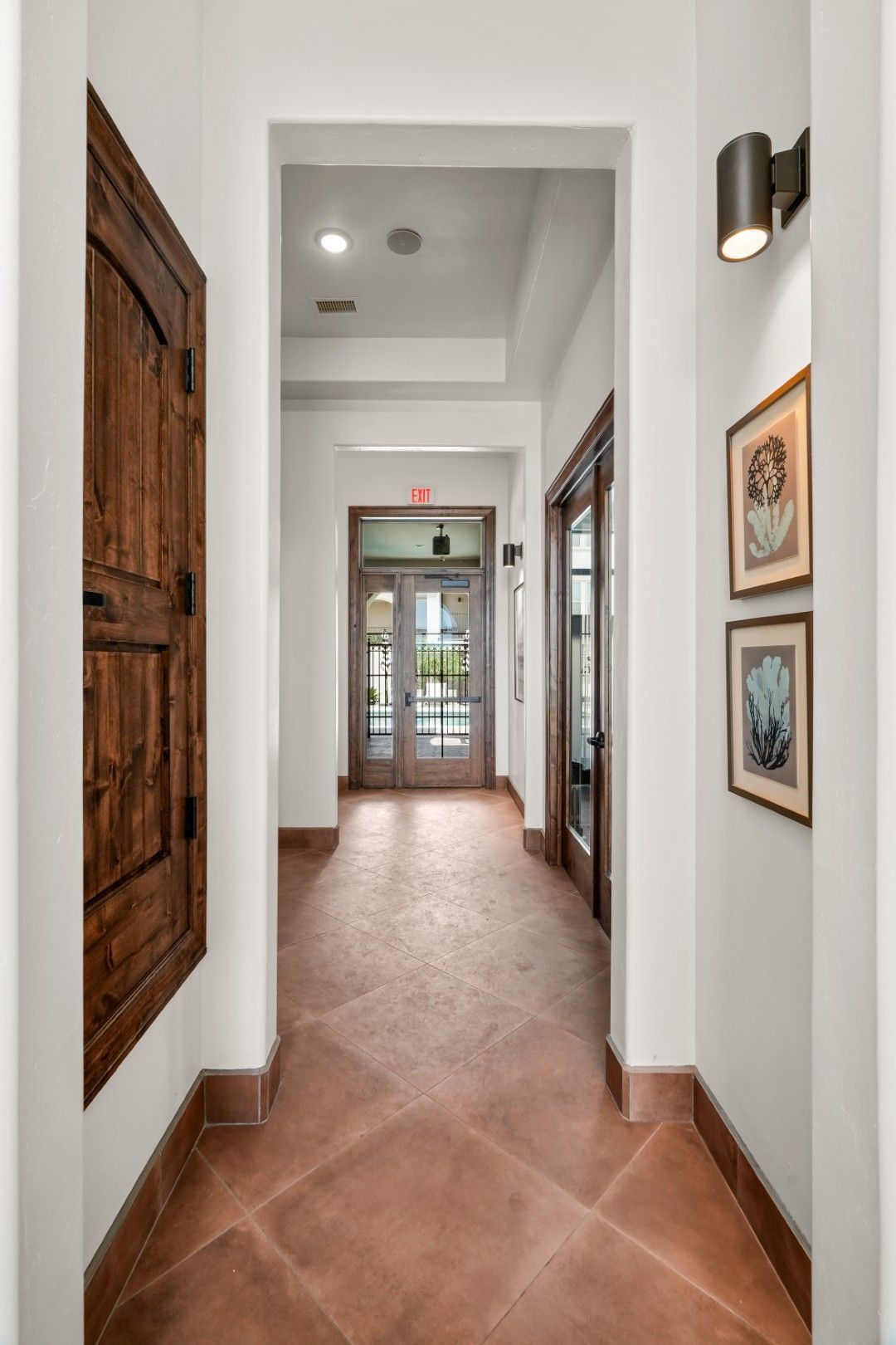 A hallway with a tiled floor and wooden doors leading to a doorway.