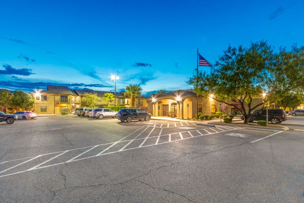 A parking lot with cars parked in front of a building at night.