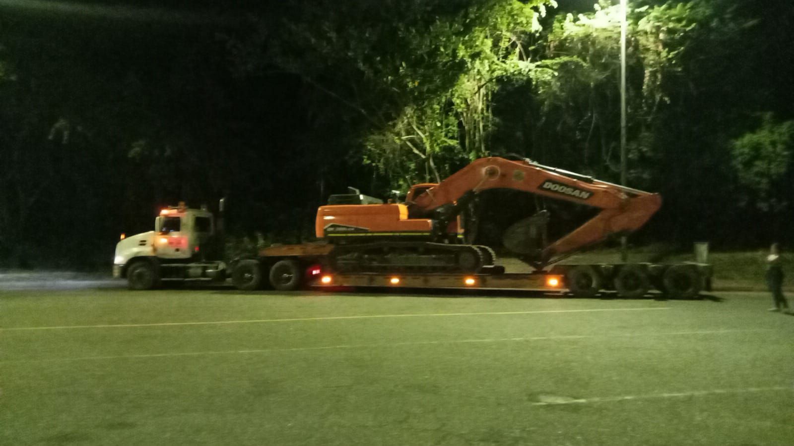 Un camión transporta una gran excavadora en un remolque por la noche.
